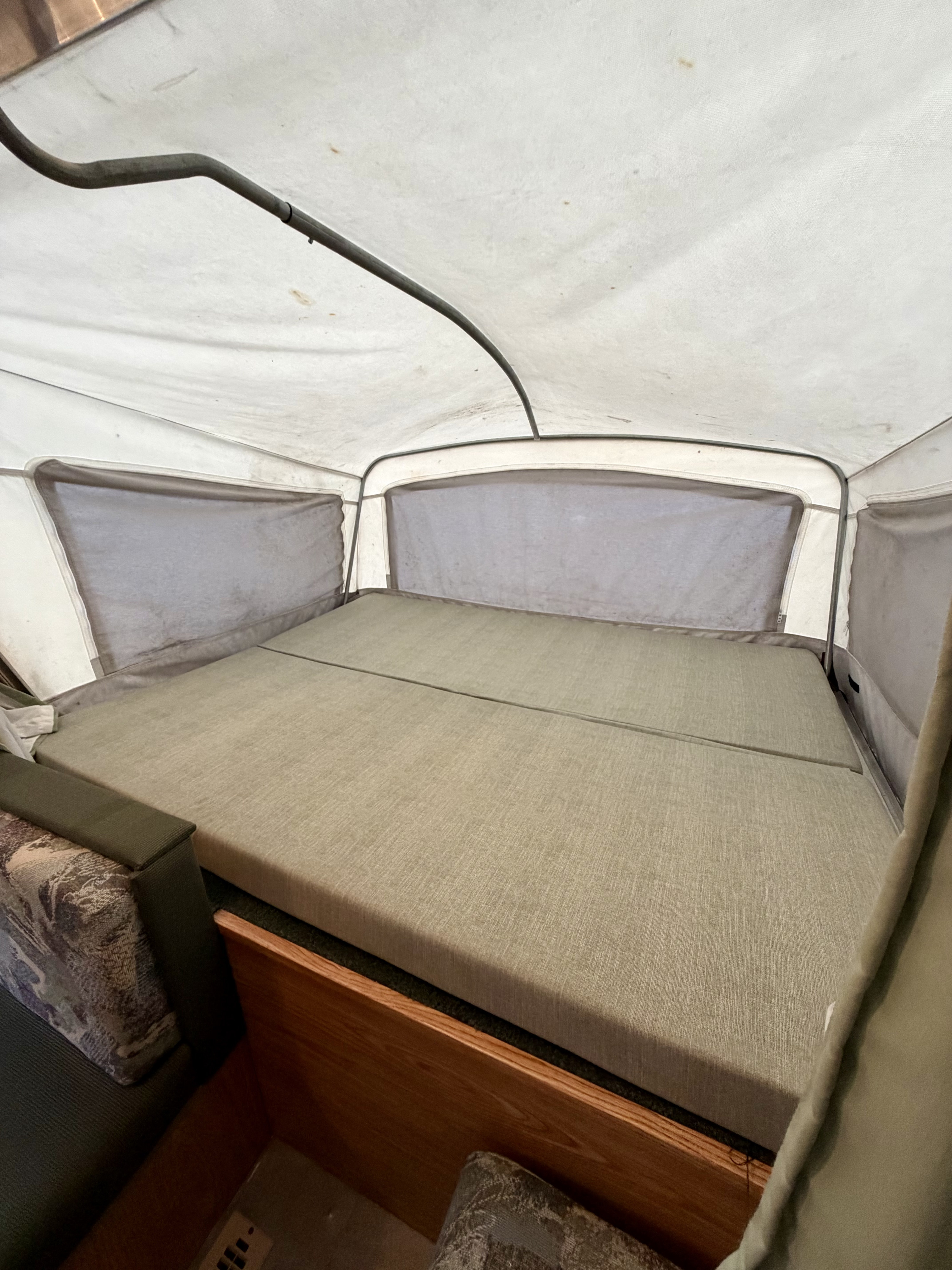 Interior of an rv rental pop-up camper, featuring a neutral-toned bed, canvas walls, and structural support poles.. Dutchmen Sport 2003