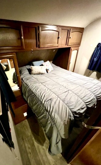 Comfortable RV rental bedroom with wood cabinets, a bed with gray comforter, and built-in mirror panels.. Forest River Freedom 2017