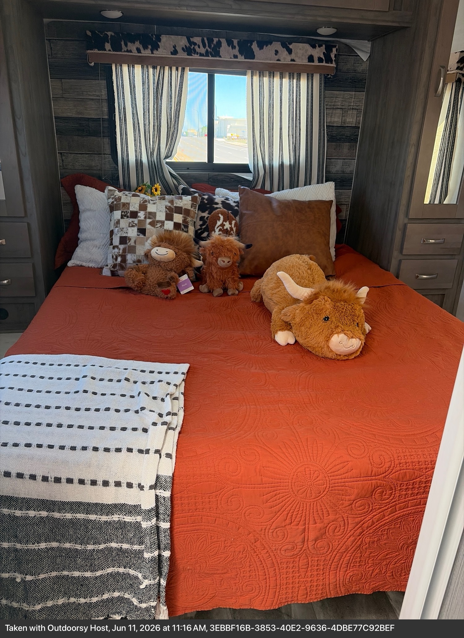 Cozy RV rental bedroom with orange quilt, highland cow plushies, and western-themed decor by the window.. Conquest 6280D 2024