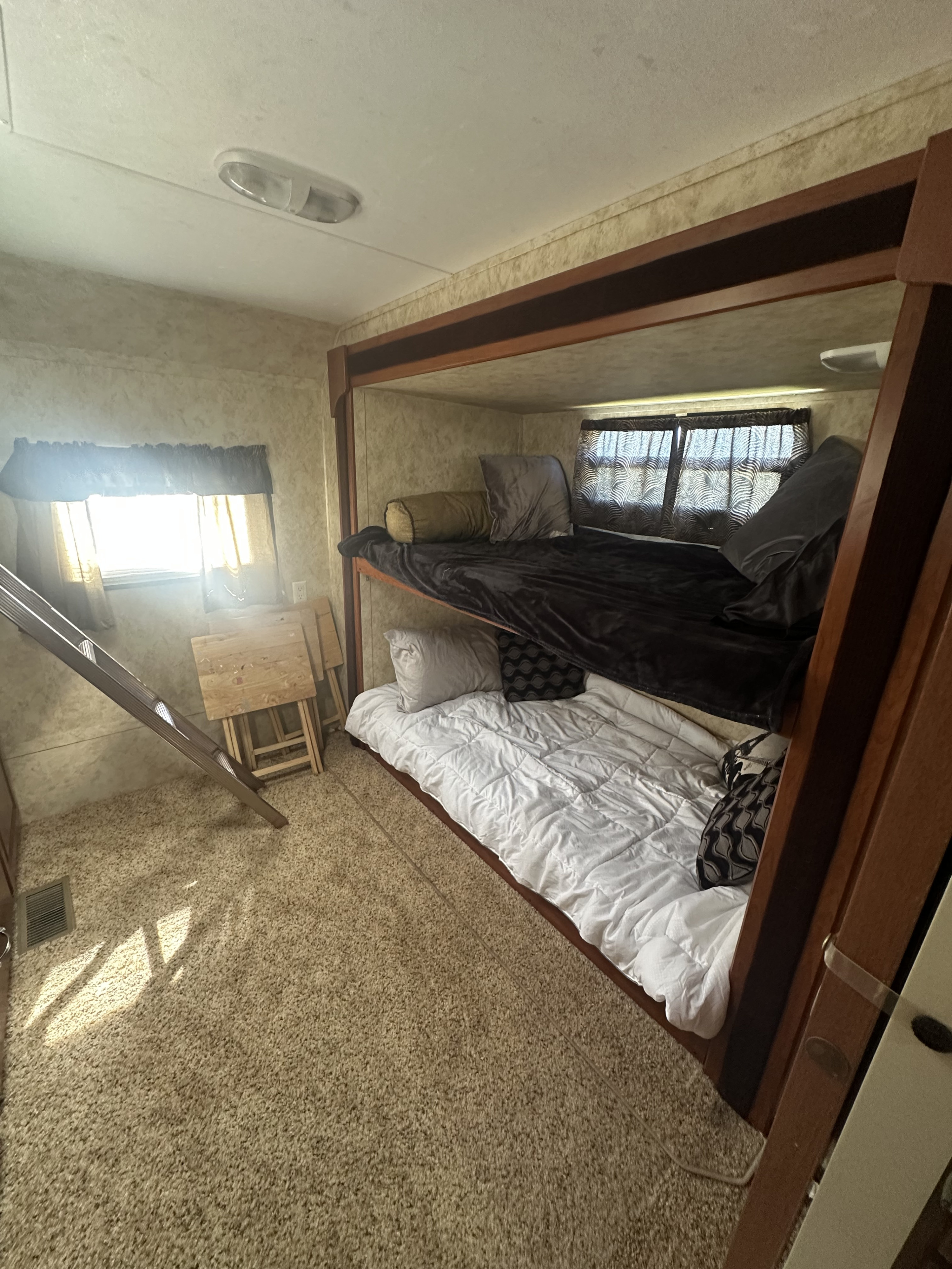 Inside an RV rental, showing bunk beds with blankets, a ladder, and carpeted floor, bathed in sunlight.. Keystone cougar cougar 2010