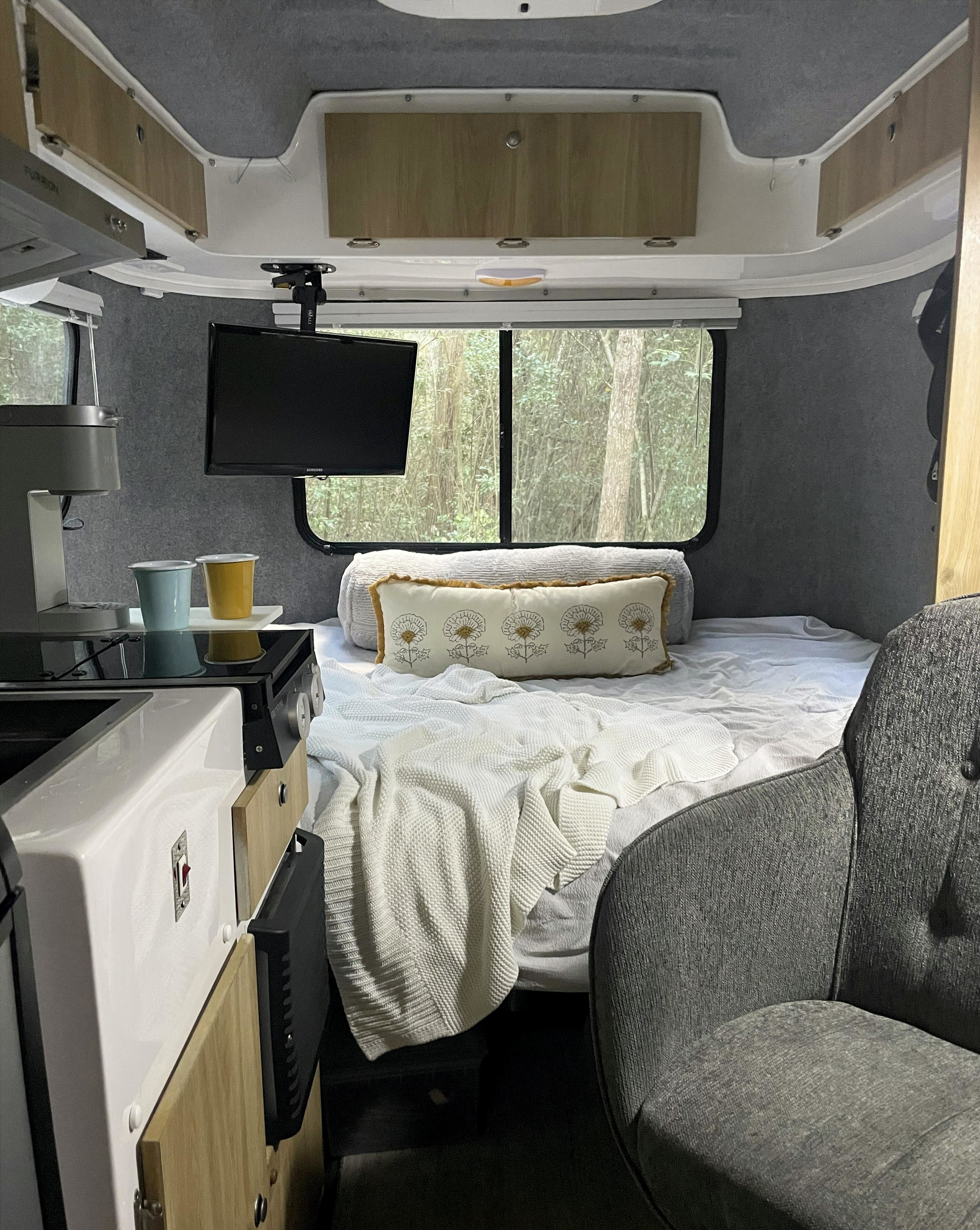 Cozy rv rental interior with bed, kitchen, TV, and forest view from window. Perfect for adventure!. Casita Freedom 2024