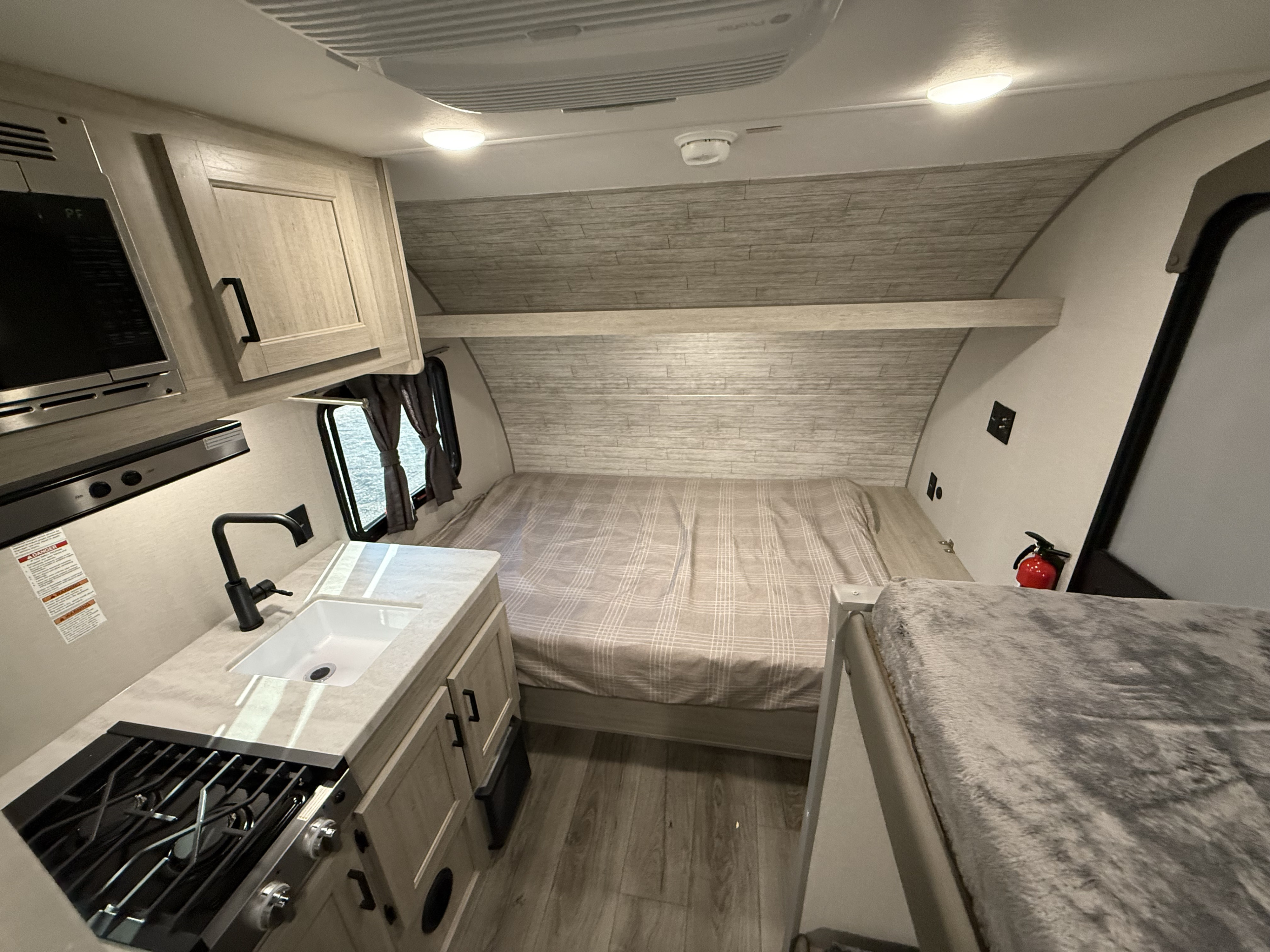 Spacious RV rental interior featuring a full kitchen with stove and sink, a main bed, and a cozy overhead bunk.. Coachmen catalina 2025