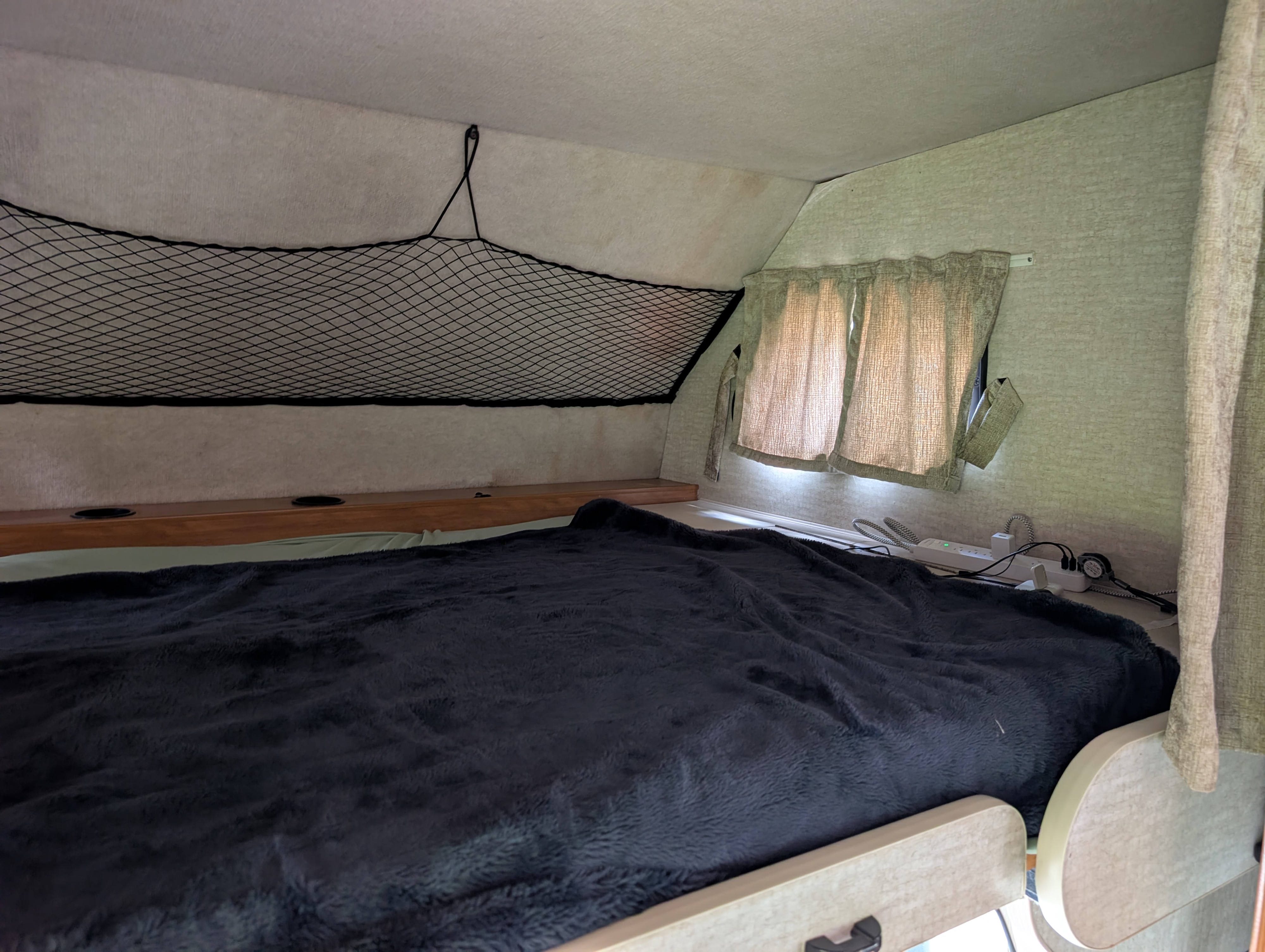 Inside an RV rental: a comfortable bed with a plush blanket, overhead storage net, and bedside charging station.. Tioga Tioga Motorhome 2008