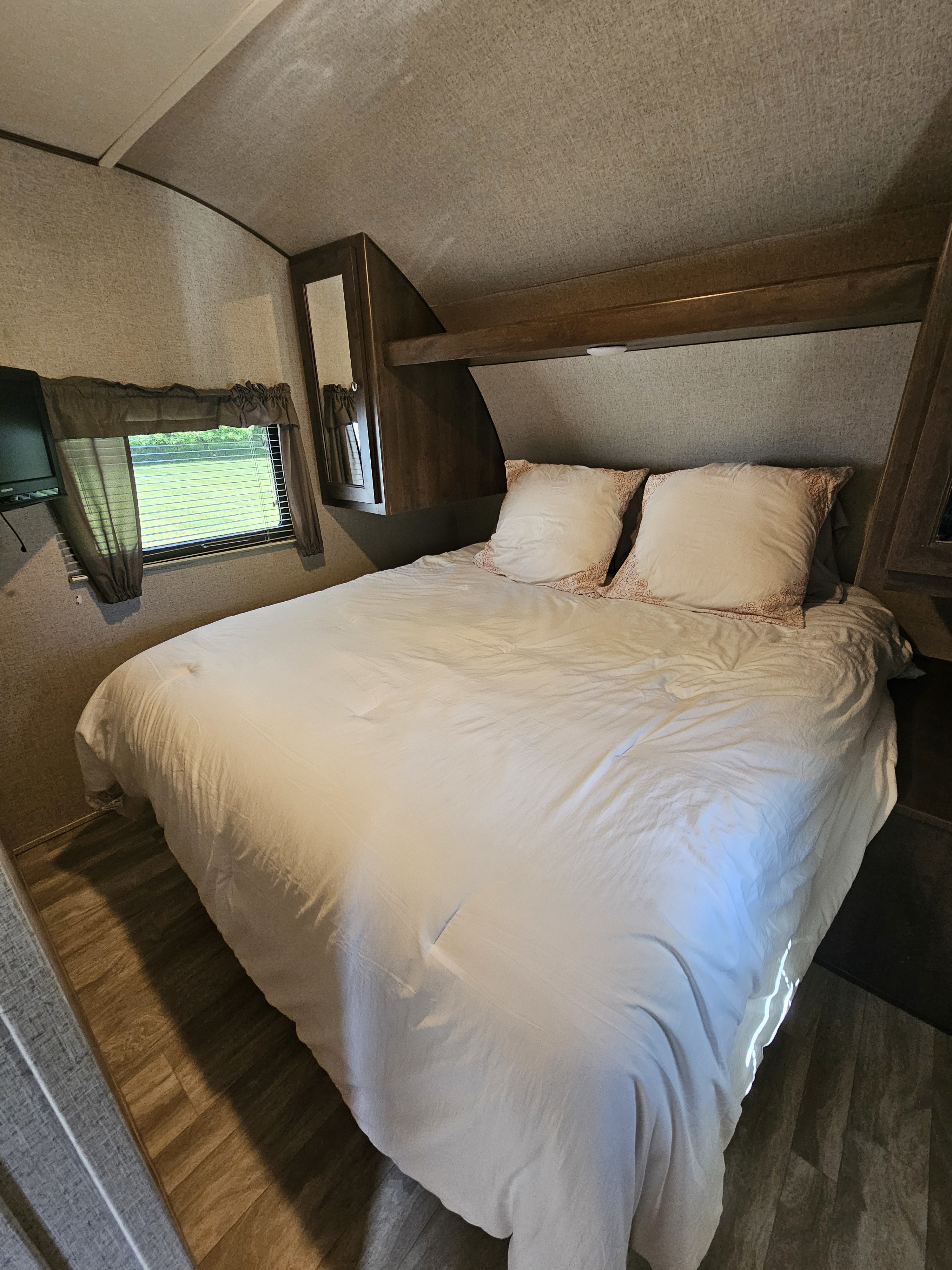 Cozy RV rental bedroom with a neatly made bed, white bedding, window view, and practical overhead storage.. Shasta Oasis 2018