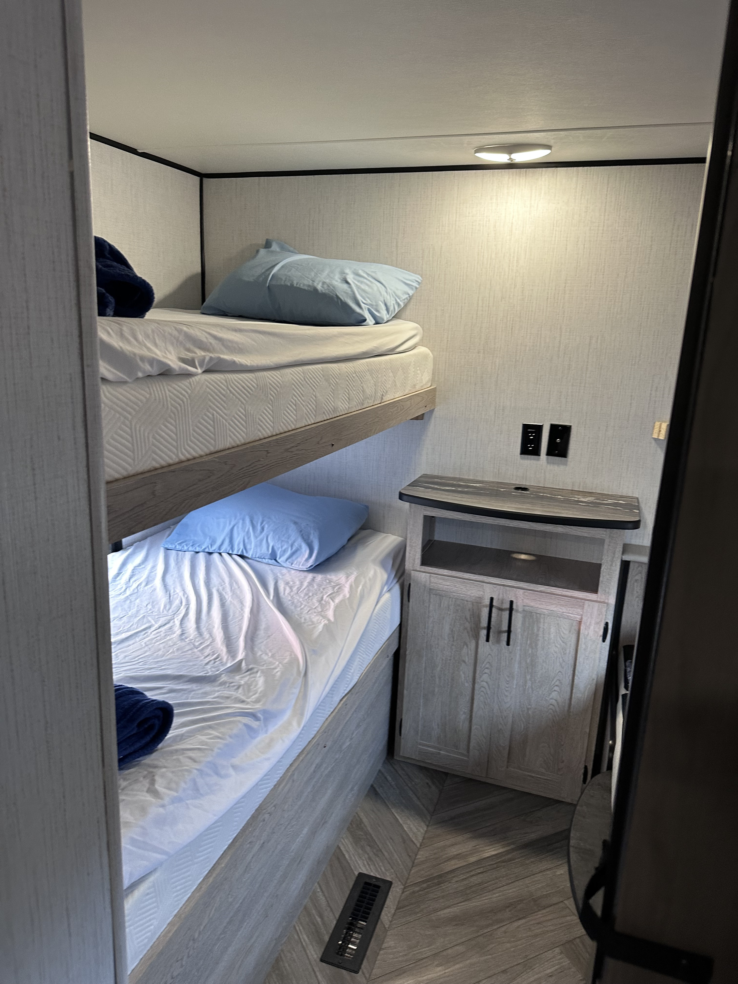 RV rental bunk beds in a modern camper interior, featuring blue pillows, a cabinet, and power outlets.. Heartland RVs Prowler 2022