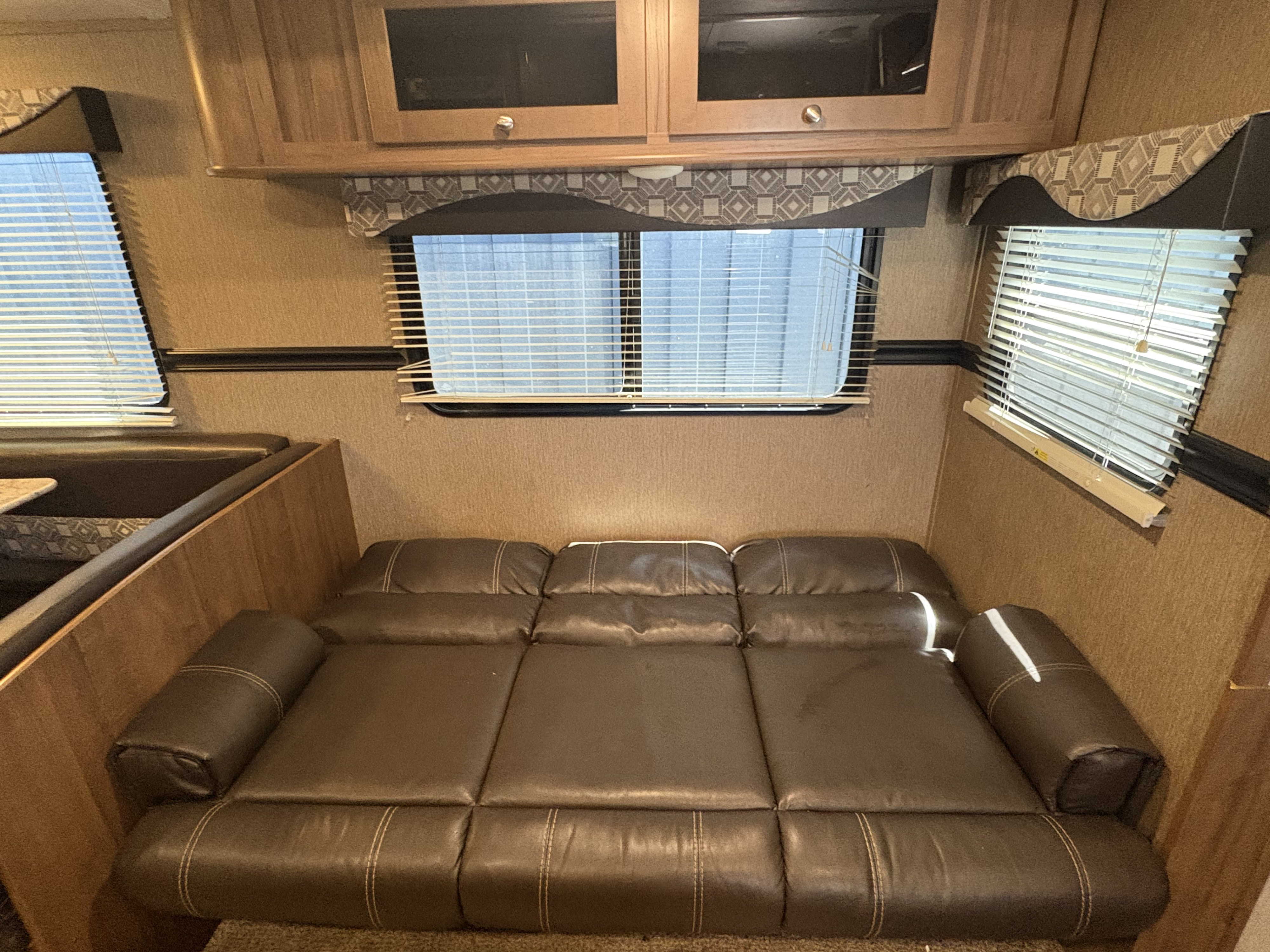 RV rental interior featuring a brown leather sofa bed, windows with blinds, and wooden overhead cabinets.. Aspen Trail Aspen Trail Trailer 2018