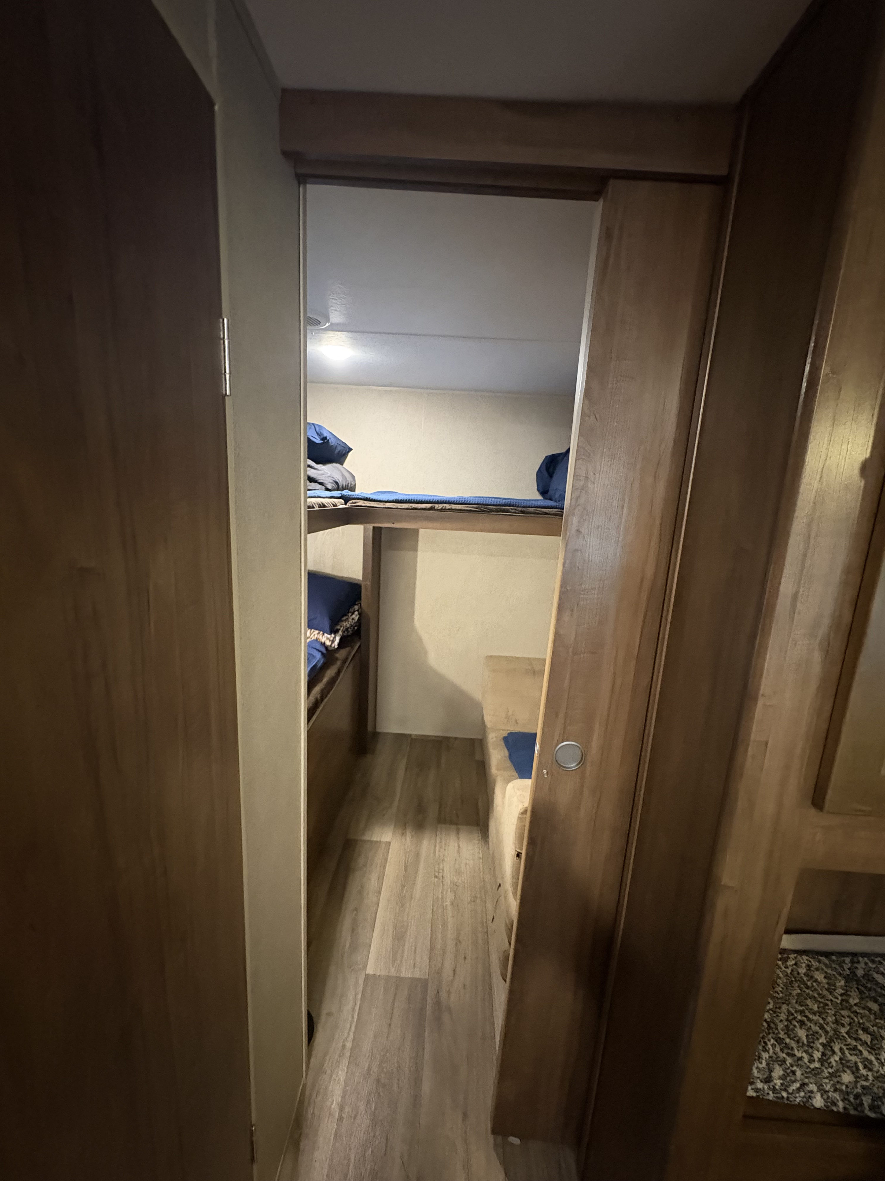 RV rental interior: narrow bunkhouse hallway with stacked beds and a small bench. Wood-look flooring, blue bedding.. Aspen Trail Aspen Trail Trailer 2018