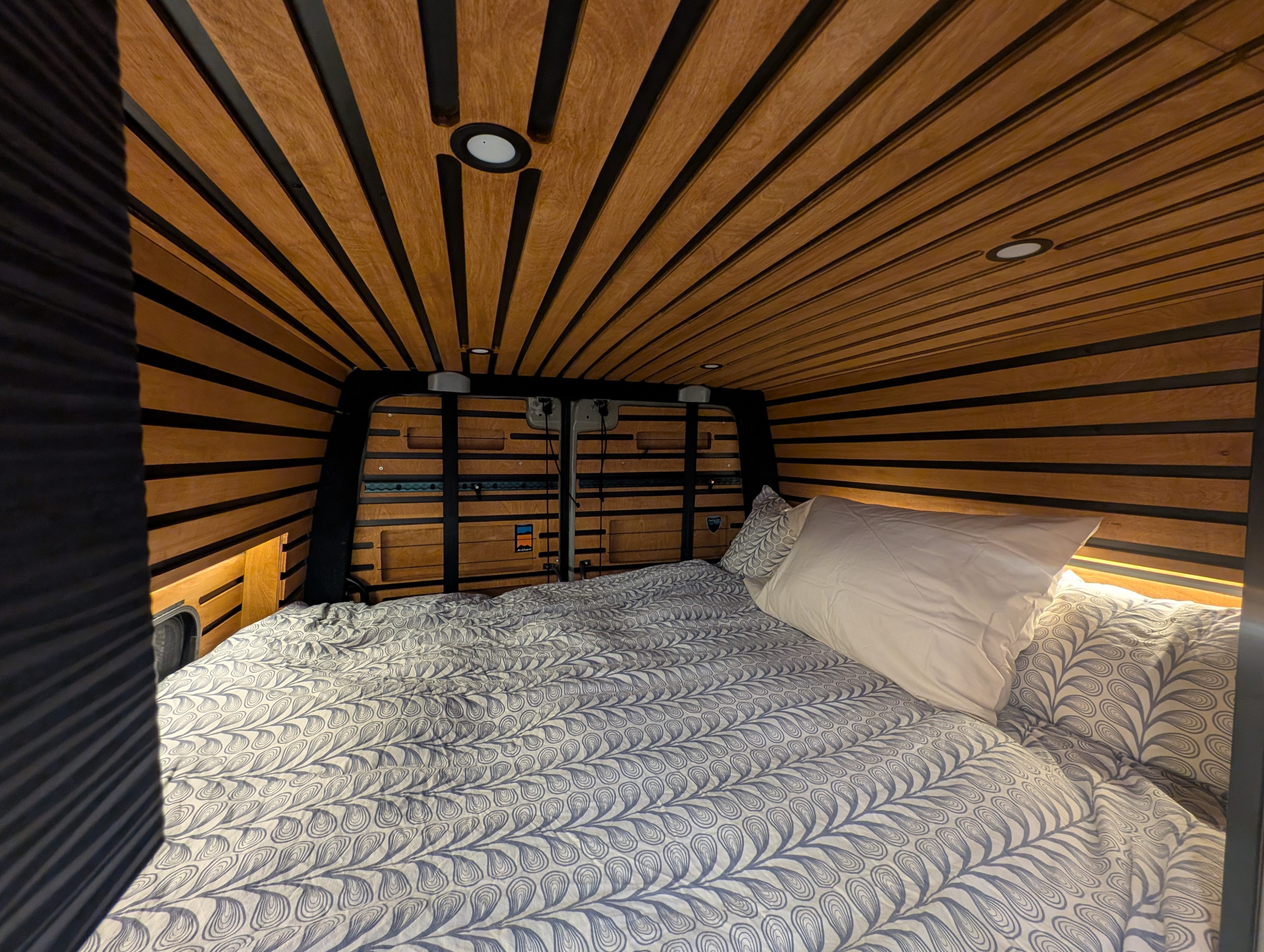 Cozy RV rental interior featuring a comfortable bed with patterned bedding, warm wood paneling, and recessed lighting.. Mercedes-Benz Sprinter RV Motorhome Campervan 2023