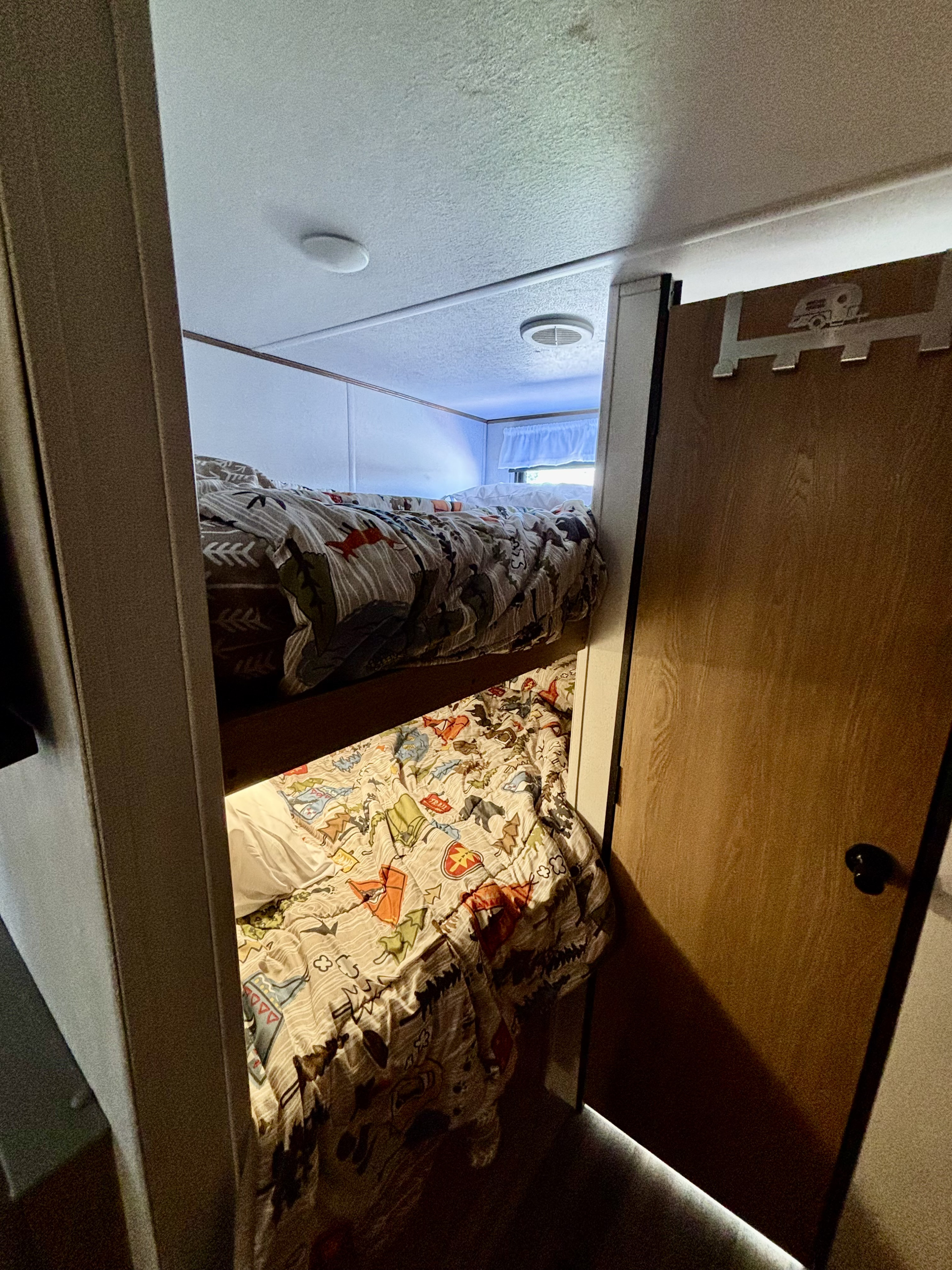 Bunk beds in an rv rental, showcasing colorful, themed comforters and soft accent lighting under the top bunk.. Avenger LT 2022
