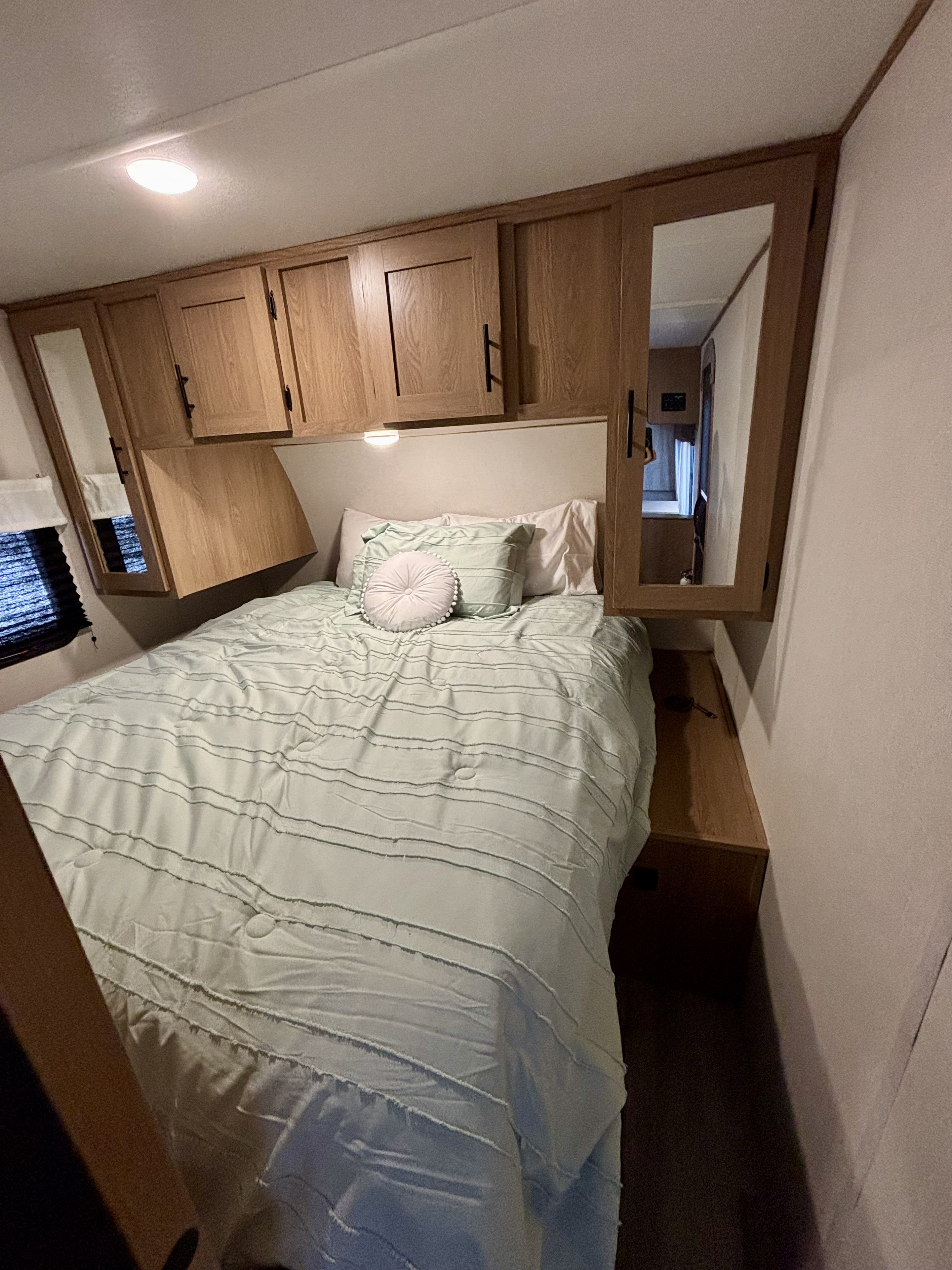 Cozy rv rental bedroom: light blue bed, wooden overhead cabinets with mirrors, and built-in lighting for comfort.. Avenger LT 2022