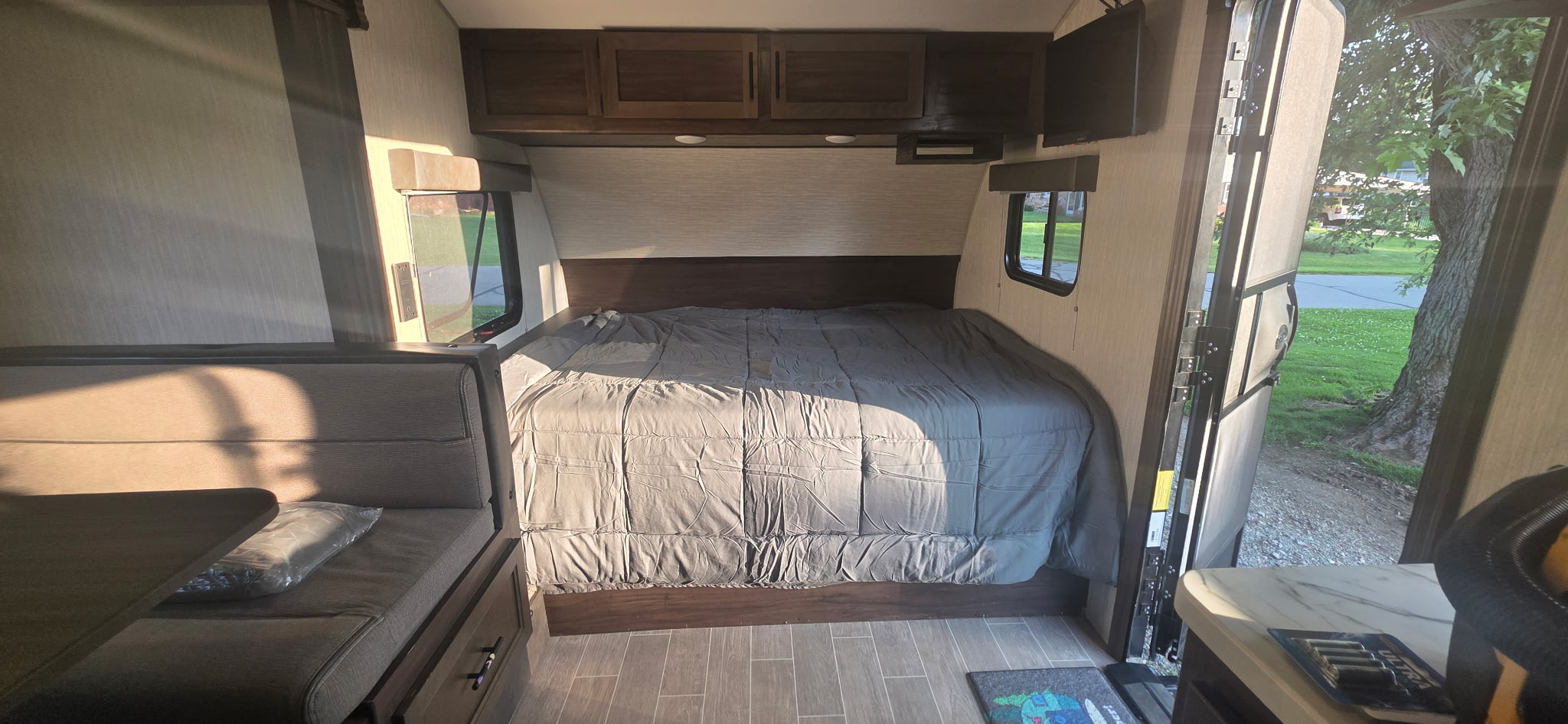 Inside an RV rental, showing a comfortable bed, dinette area, and sunny view of the outdoors from an open door.. Forest River Cherokee Wolf Pup 2019