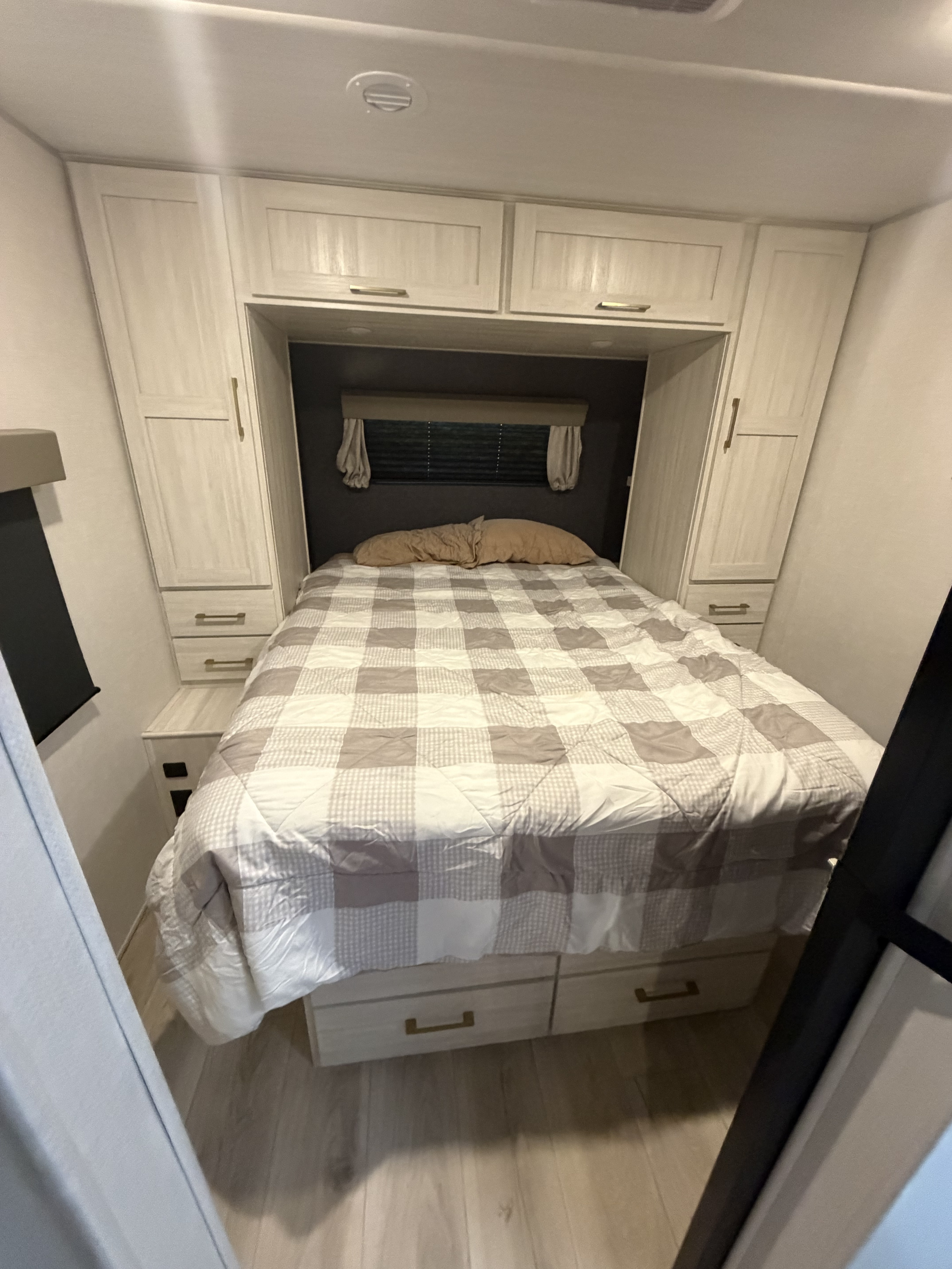 Cozy RV rental bedroom features a comfy bed with a gray and white checkered comforter, built-in storage, and ambient lighting.. Forest River Surveyor Legend 2024