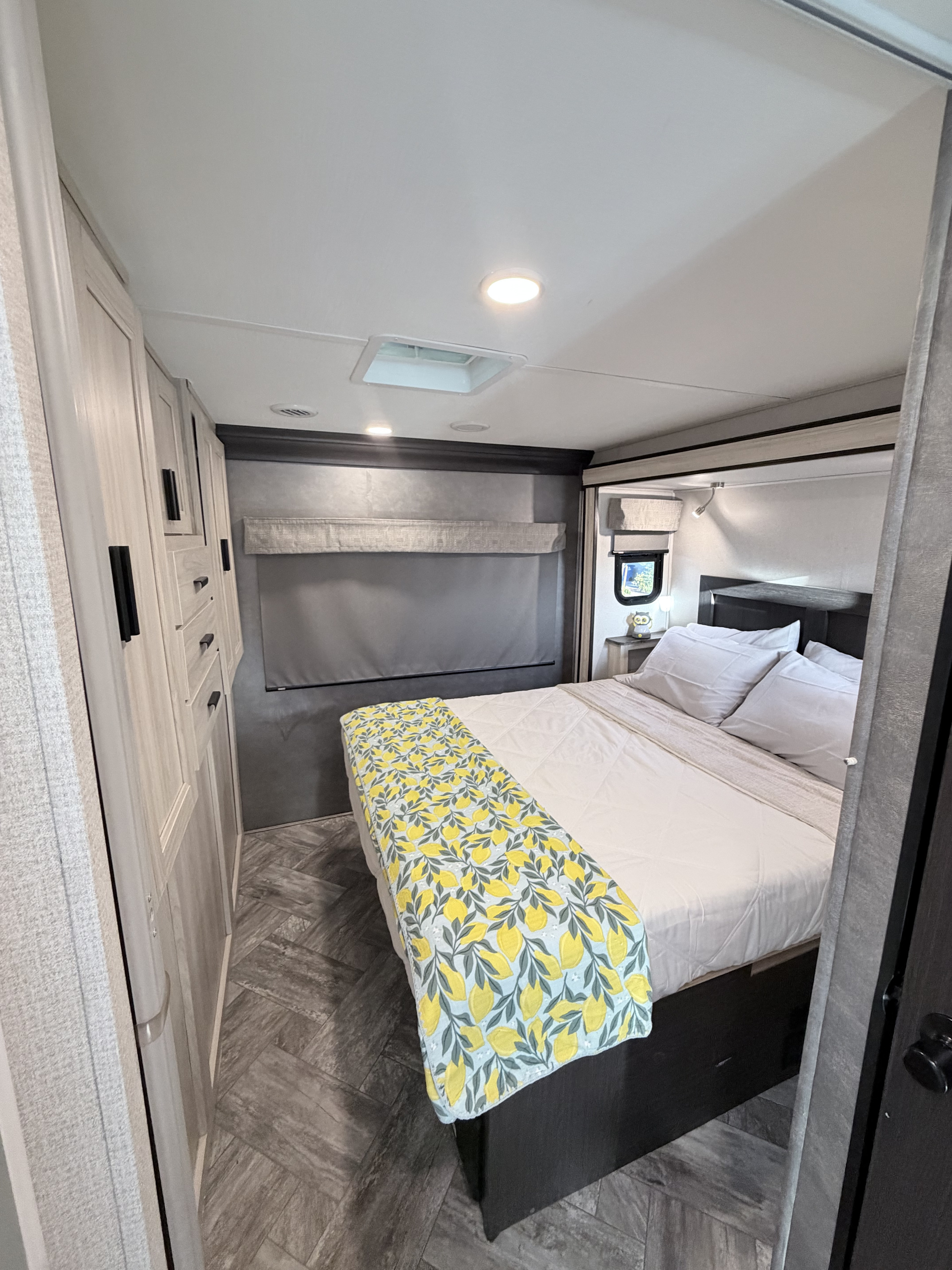 Spacious RV rental bedroom with a white bed, yellow lemon blanket, light wood cabinets, and dark patterned floor.. Forest River Sunseeker Classic 2023