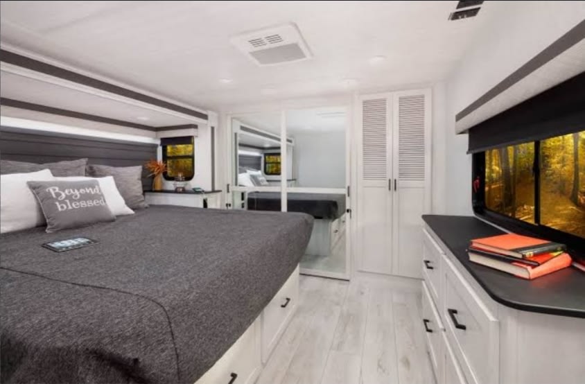 Modern RV rental bedroom featuring a spacious bed, stylish gray and white decor, ample storage, and scenic window views.. East to West Ahara 2022