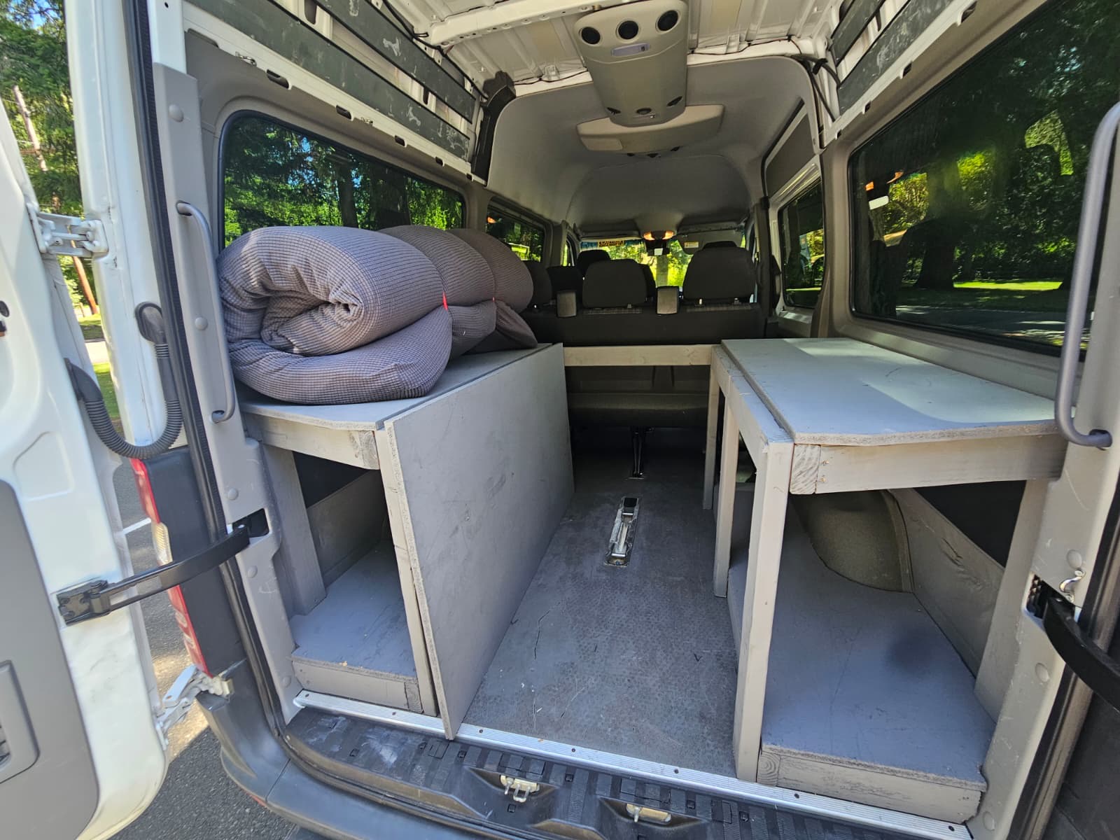 RV rental: Inside a camper van with custom wooden storage platforms, rolled bedding, and back seats visible.. Mercedes-Benz Sprinter 2016