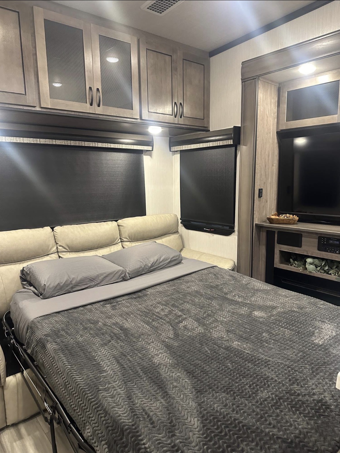 RV rental interior: a pull-out bed with grey bedding, light wood cabinets, an entertainment center with TV, and fireplace area.. Cedar Creek Cedar Creek Fifth Wheel 2022