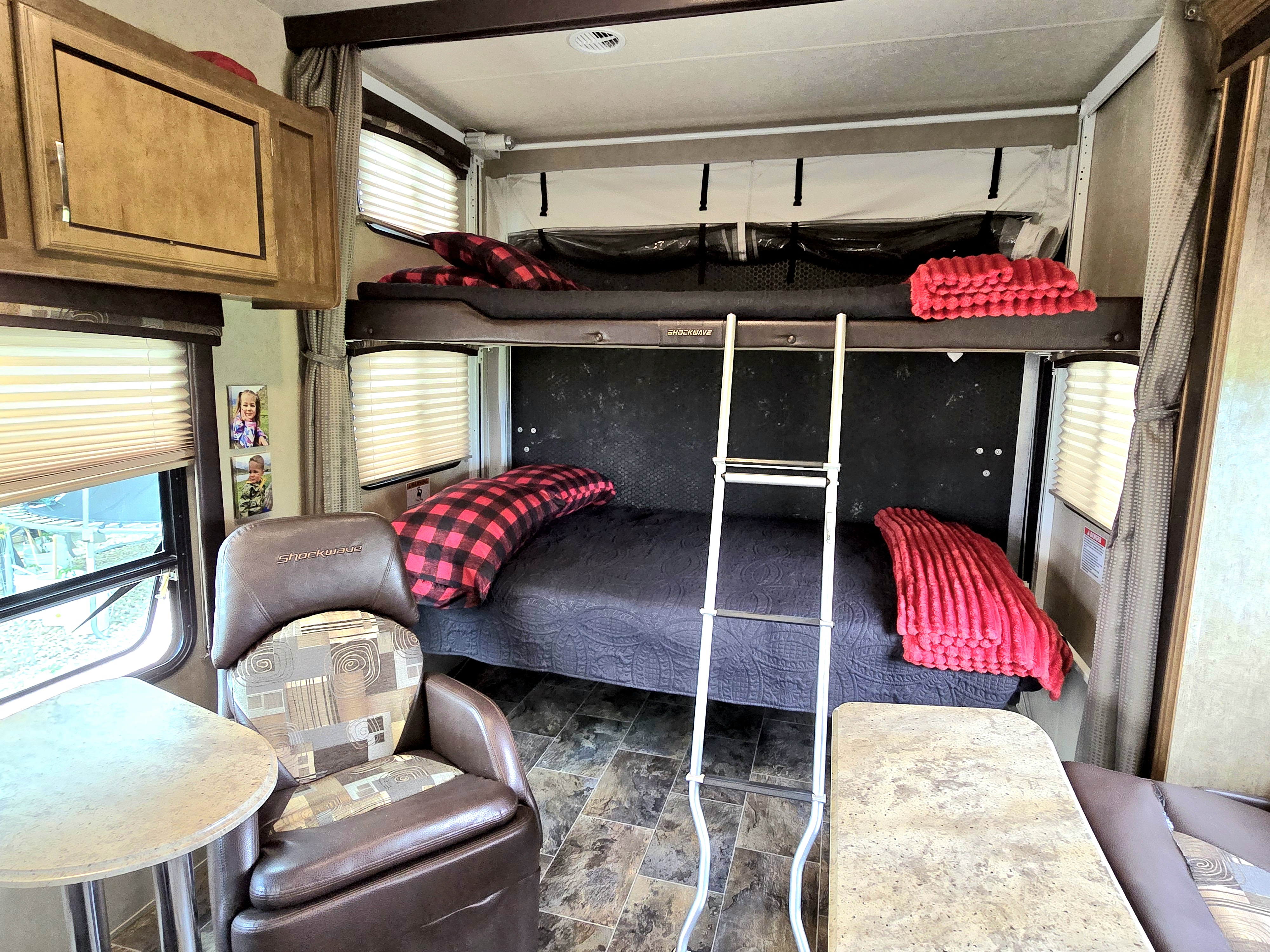 RV rental interior with bunk beds, ladder, armchair, and table. Photos of children adorn the wall, adding a personal touch.. Forest River Shockwave 2017