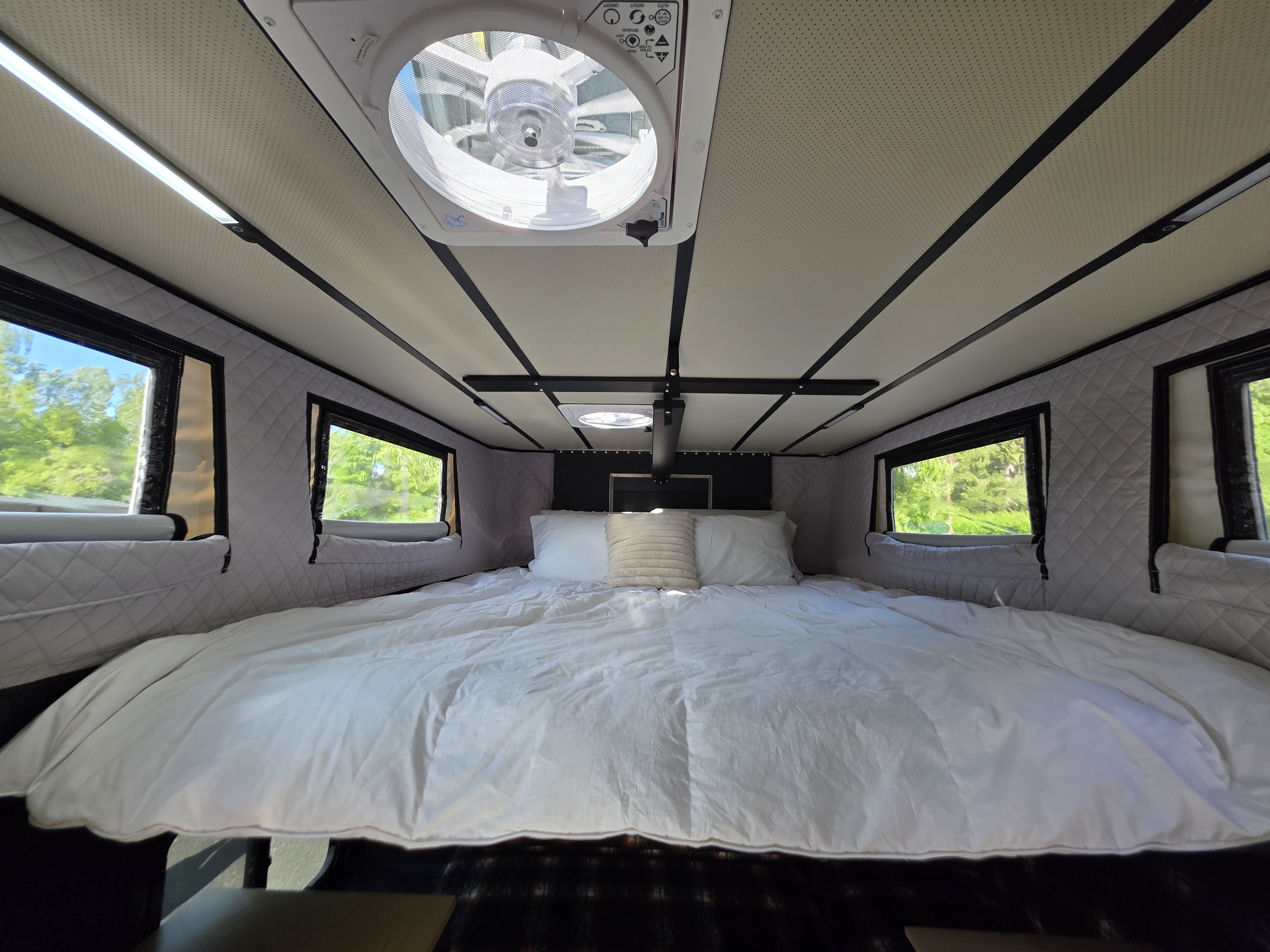 Cozy RV rental bedroom featuring a spacious bed, ambient lighting, windows with scenic views, and a ceiling fan.. Ford F350 2025
