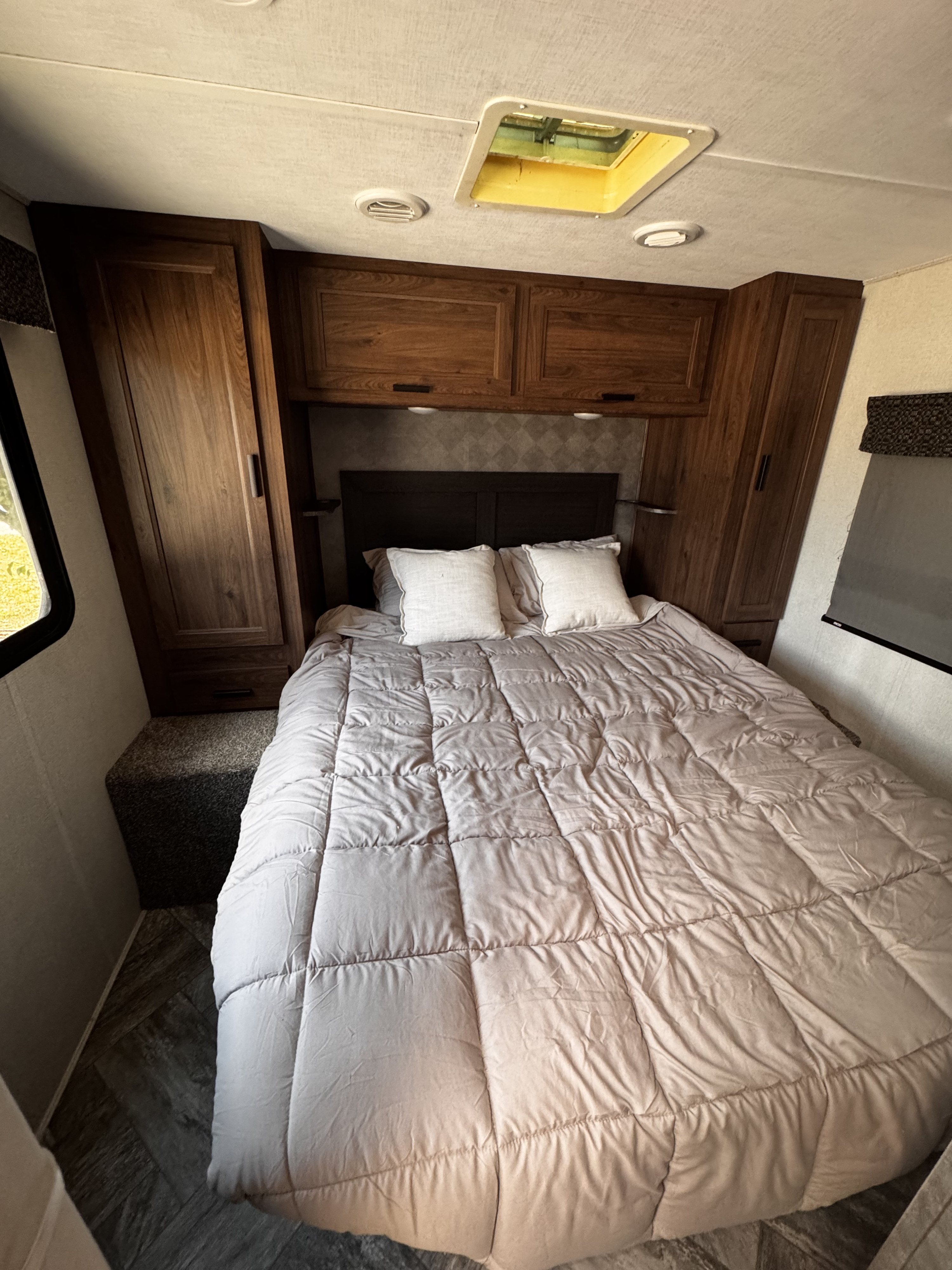 A comfortable RV rental bedroom with a bed, overhead storage, side wardrobes, and a window, ideal for travel.. Forest River Sunseeker LE 2021