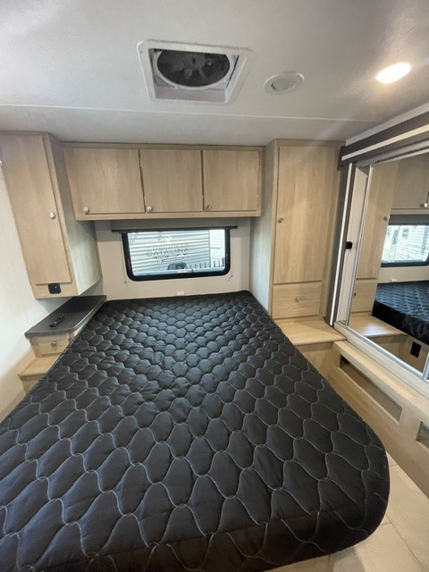 RV rental bedroom features a comfy black quilted mattress, light wood cabinets, and a window for scenic views.. Coachmen LEPRECHAUN 319 MBF 2026