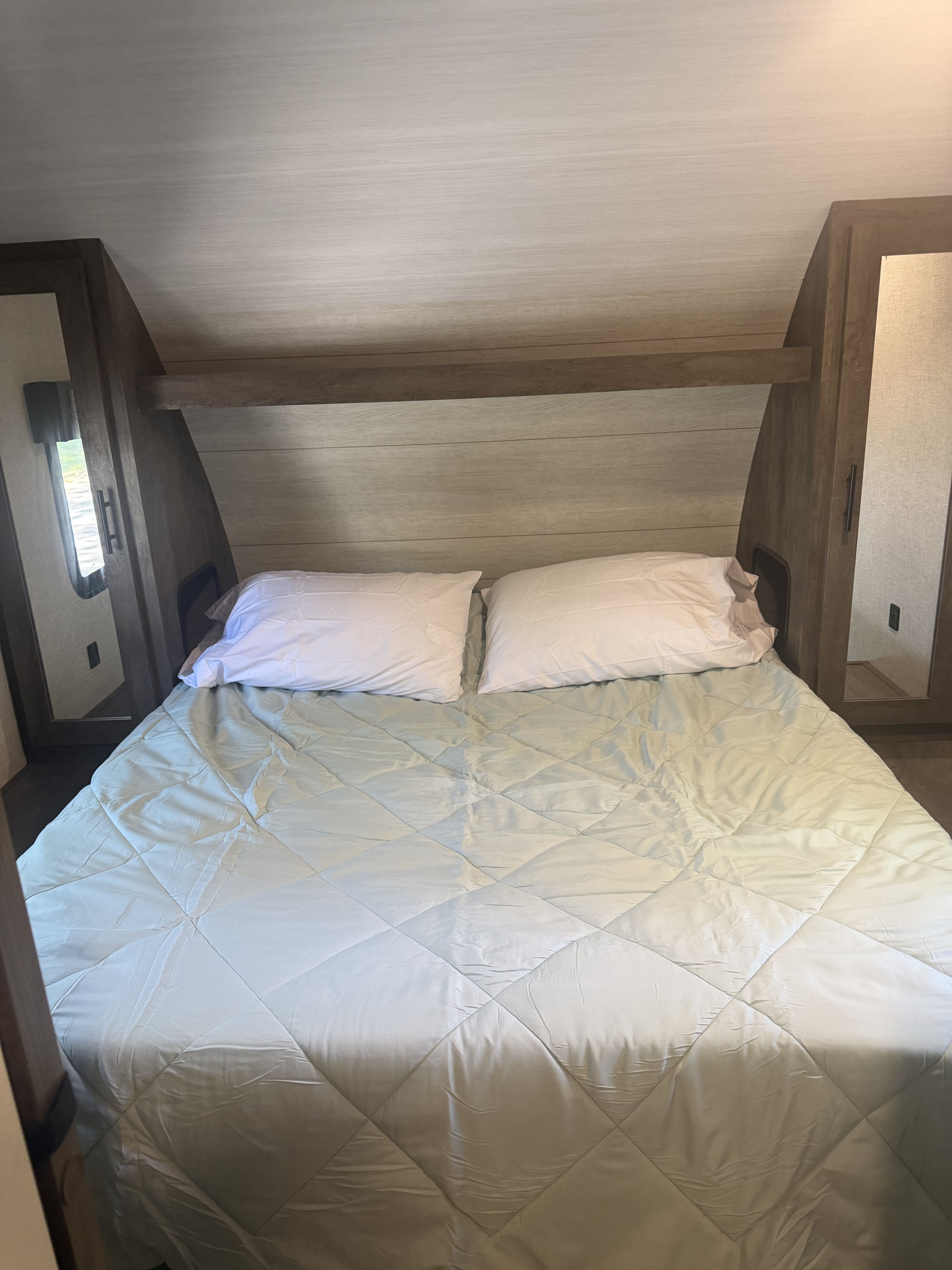 Comfortable RV rental bedroom featuring a cozy bed with white pillows and a light blue quilted comforter, flanked by built-in storage.. Forest River Wildwood X-Lite 2021