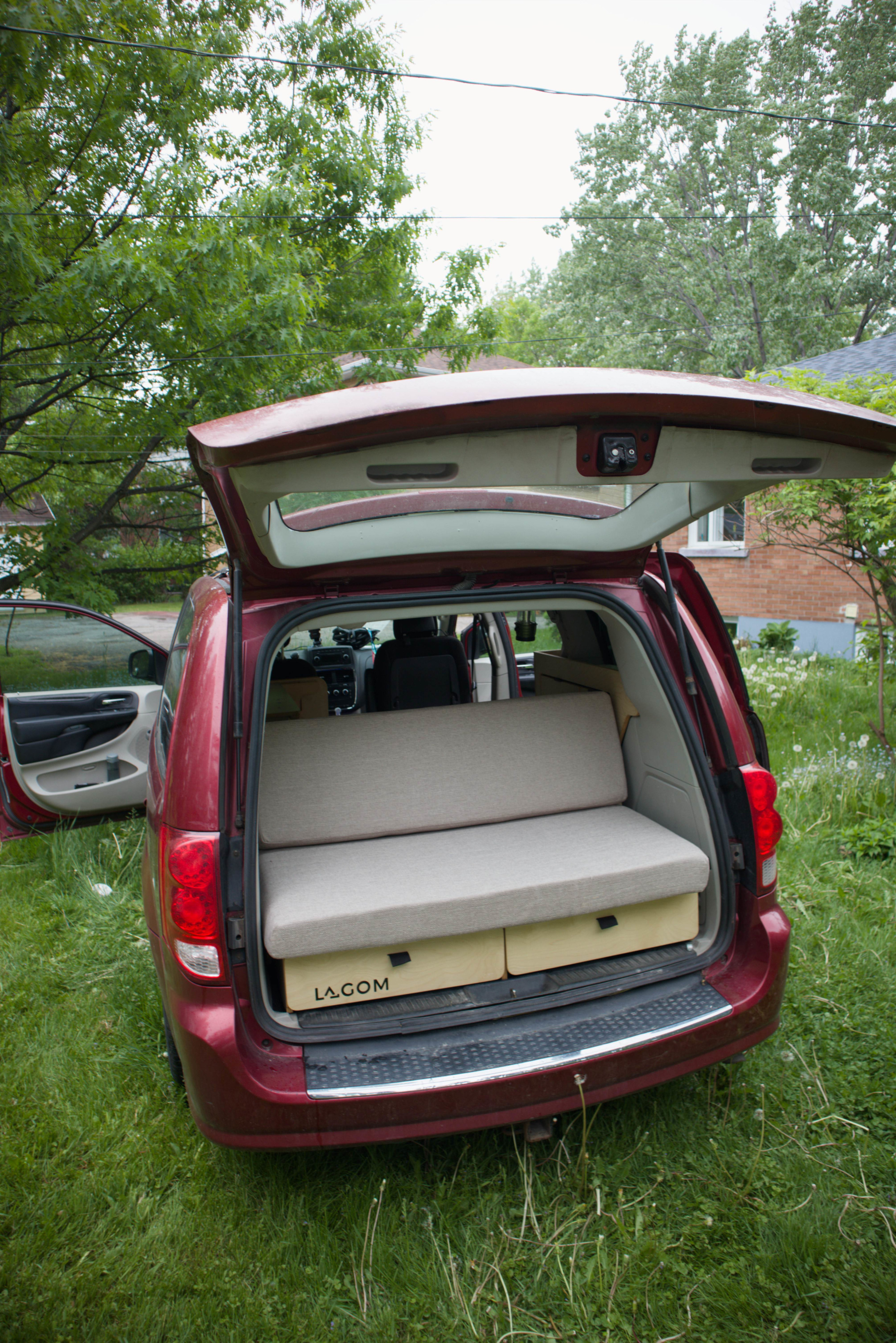 Red minivan RV rental with its tailgate open, revealing a clever modular bed and storage drawers for easy camping.. Dodge Grand Caravan 2015