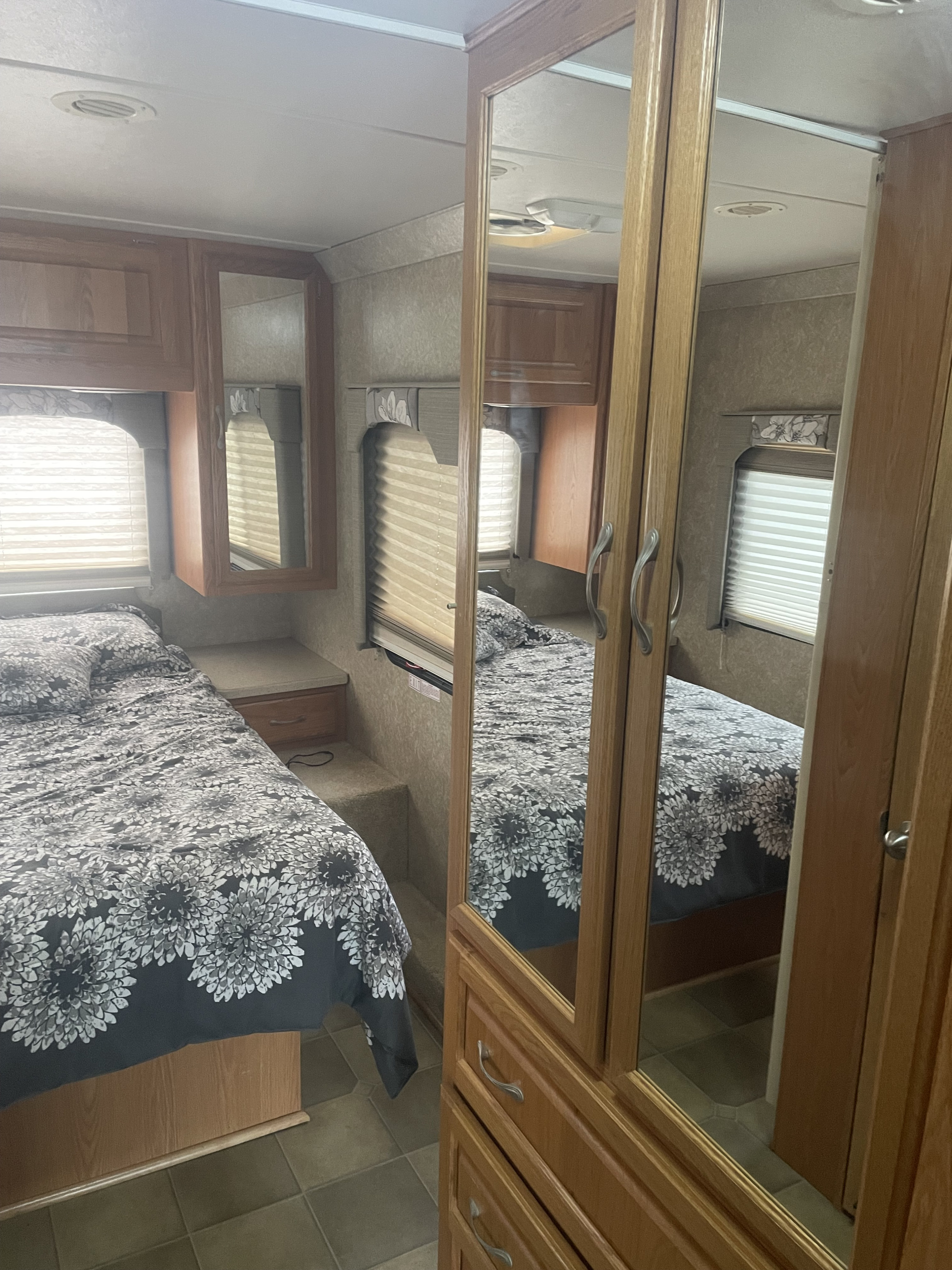 RV rental bedroom: a bed with floral duvet, window blinds, wood cabinets, and mirrored closet doors reflecting the compact space.. Thor Hurrican Four Winds M-30Q 2006