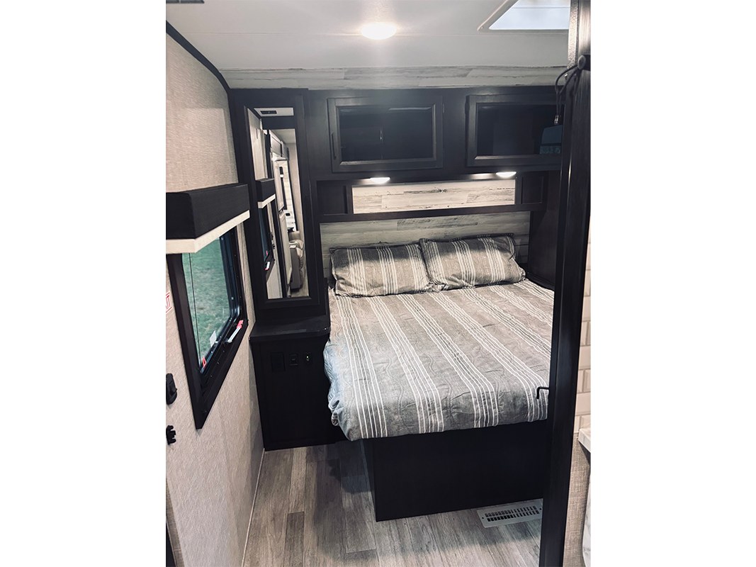 RV rental bedroom interior with a striped bed, overhead storage, and a mirror. Comfortable sleeping area.. Jayco Jay Feather 2022