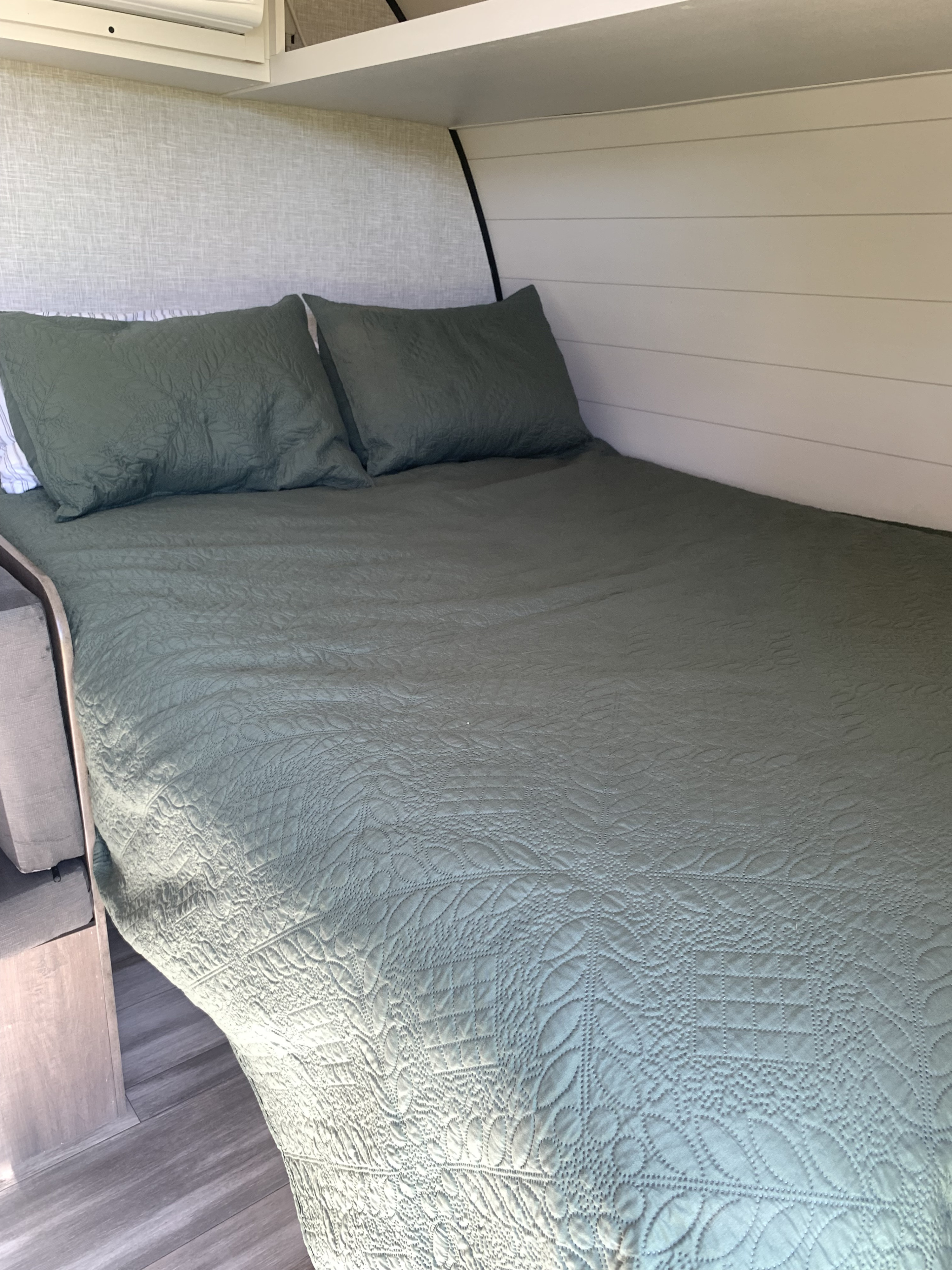 Comfortable RV rental bed featuring a green quilted cover, pillows, upholstered headboard, and shiplap walls.. Jayco Jay Flight SLX 2025
