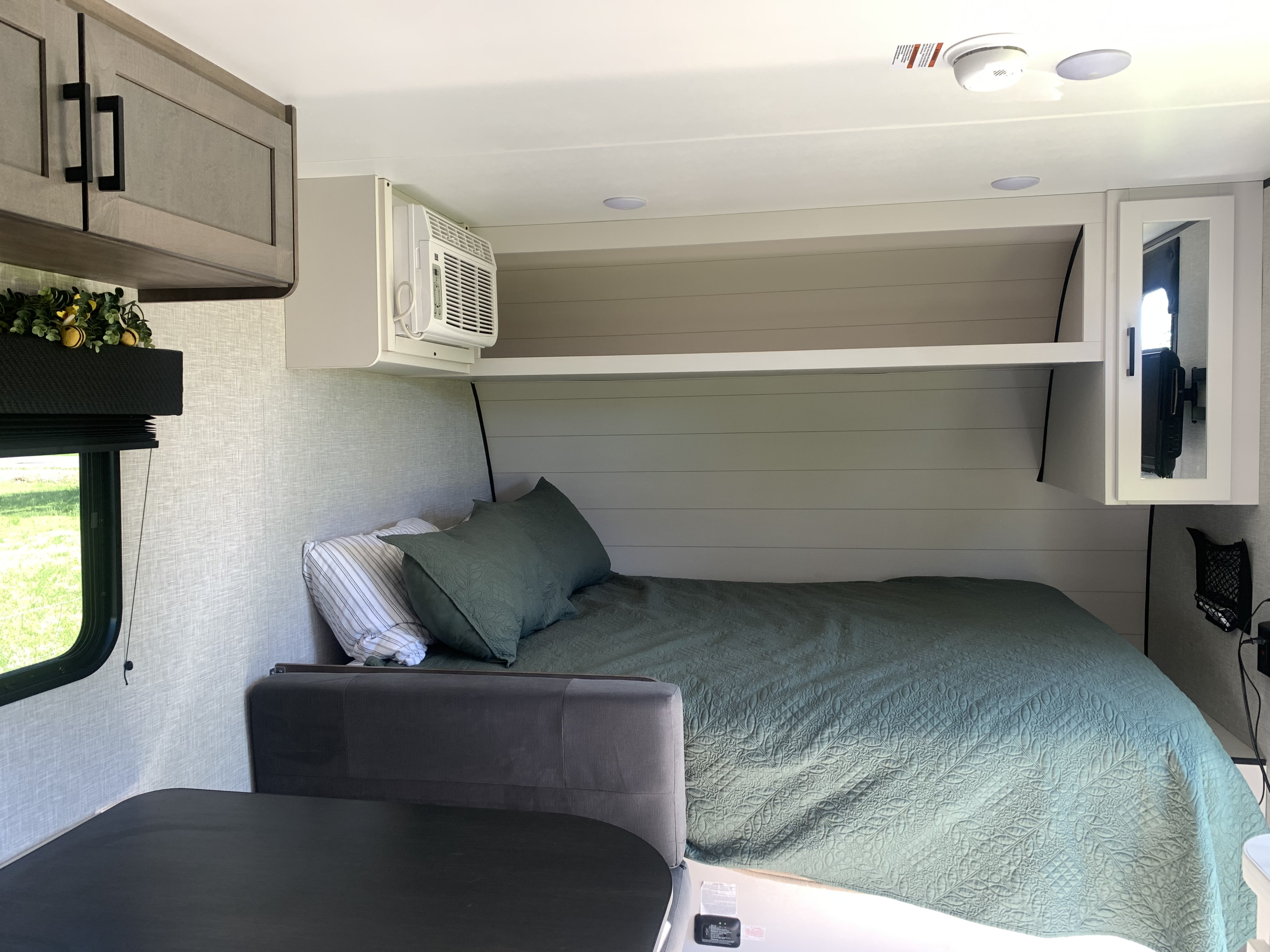 Cozy RV rental interior: a bedroom area featuring a green bed, overhead storage, window AC, and a nearby dinette.. Jayco Jay Flight SLX 2025