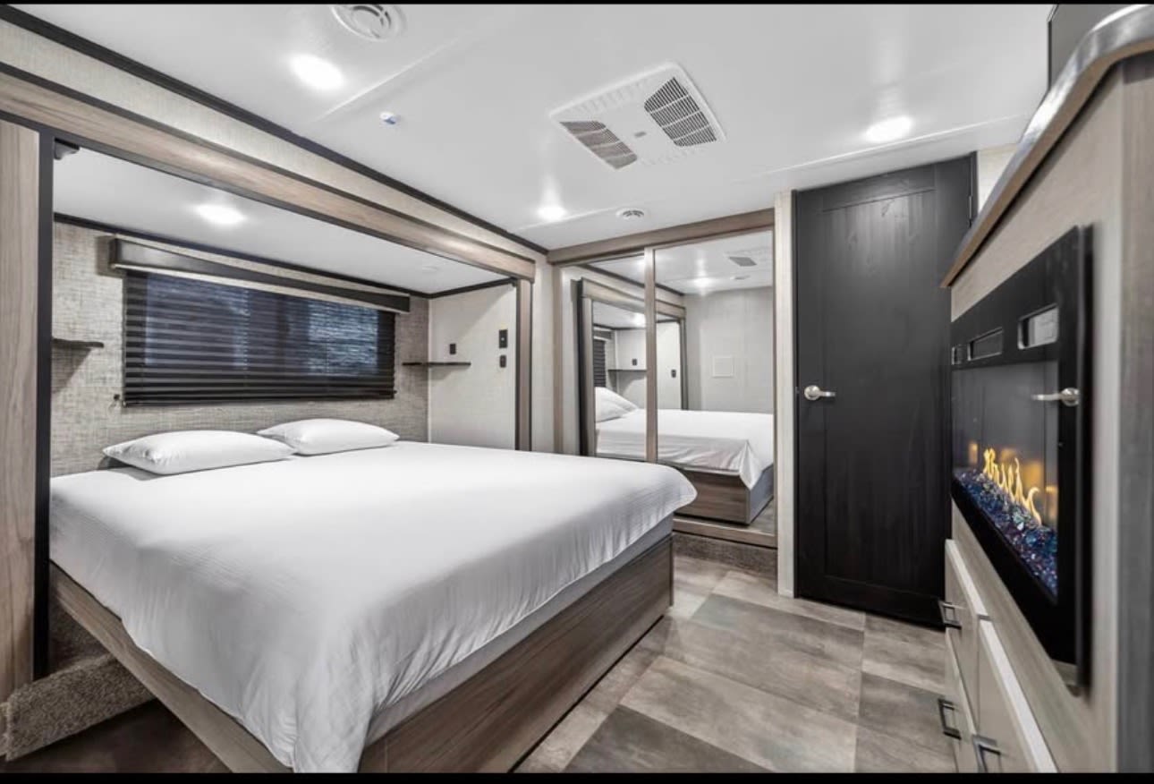 Spacious, modern RV rental bedroom with comfortable bed, mirrored closet, and electric fireplace.. Crossroads RV Cameo 2022
