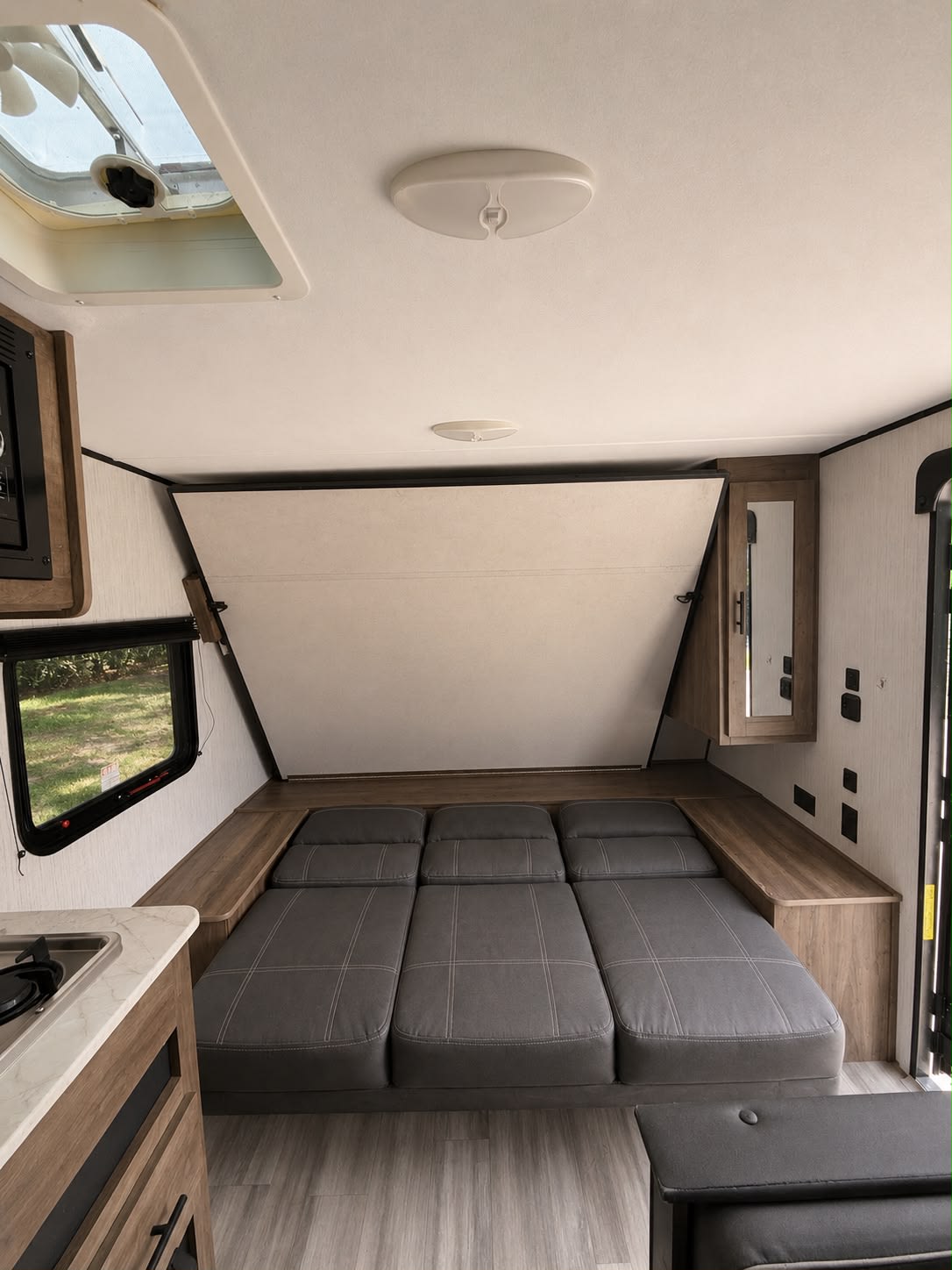 This rv rental interior features a grey convertible sofa/bed, a fold-down upper panel, and a compact kitchen counter.. Heartland BH 170 2022