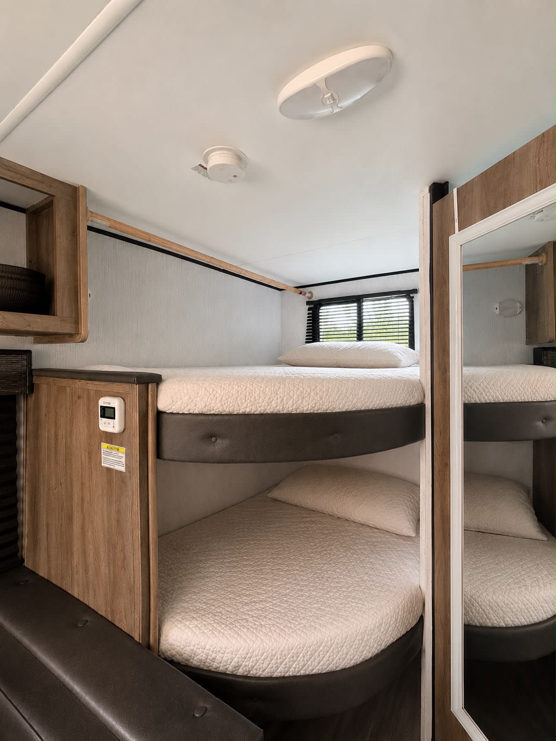 Comfortable bunk beds within an RV rental, featuring cream bedding, a window with blinds, and a thermostat on the wall.. Heartland BH 170 2022