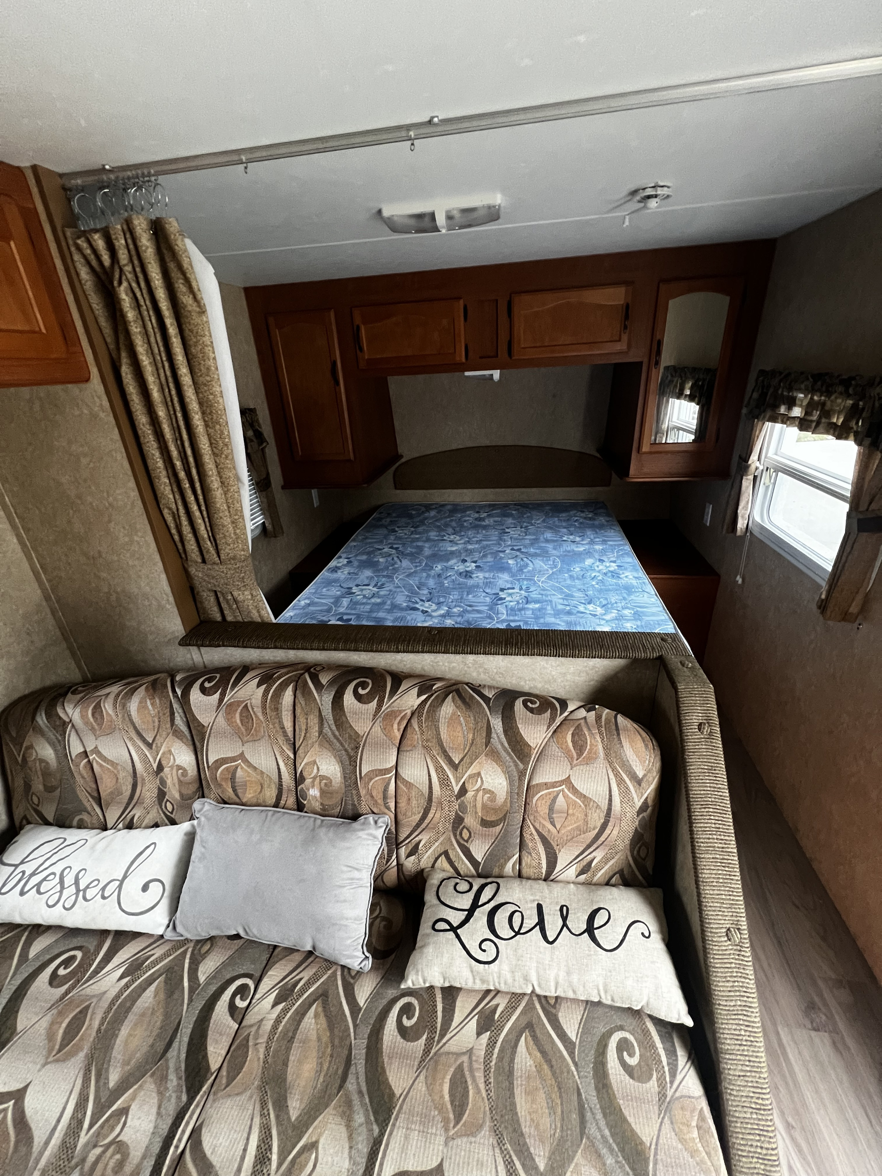 RV rental interior: A cozy dinette with "Blessed" & "Love" pillows and a bedroom area featuring a blue patterned mattress.. Forest River Wildwood 2011