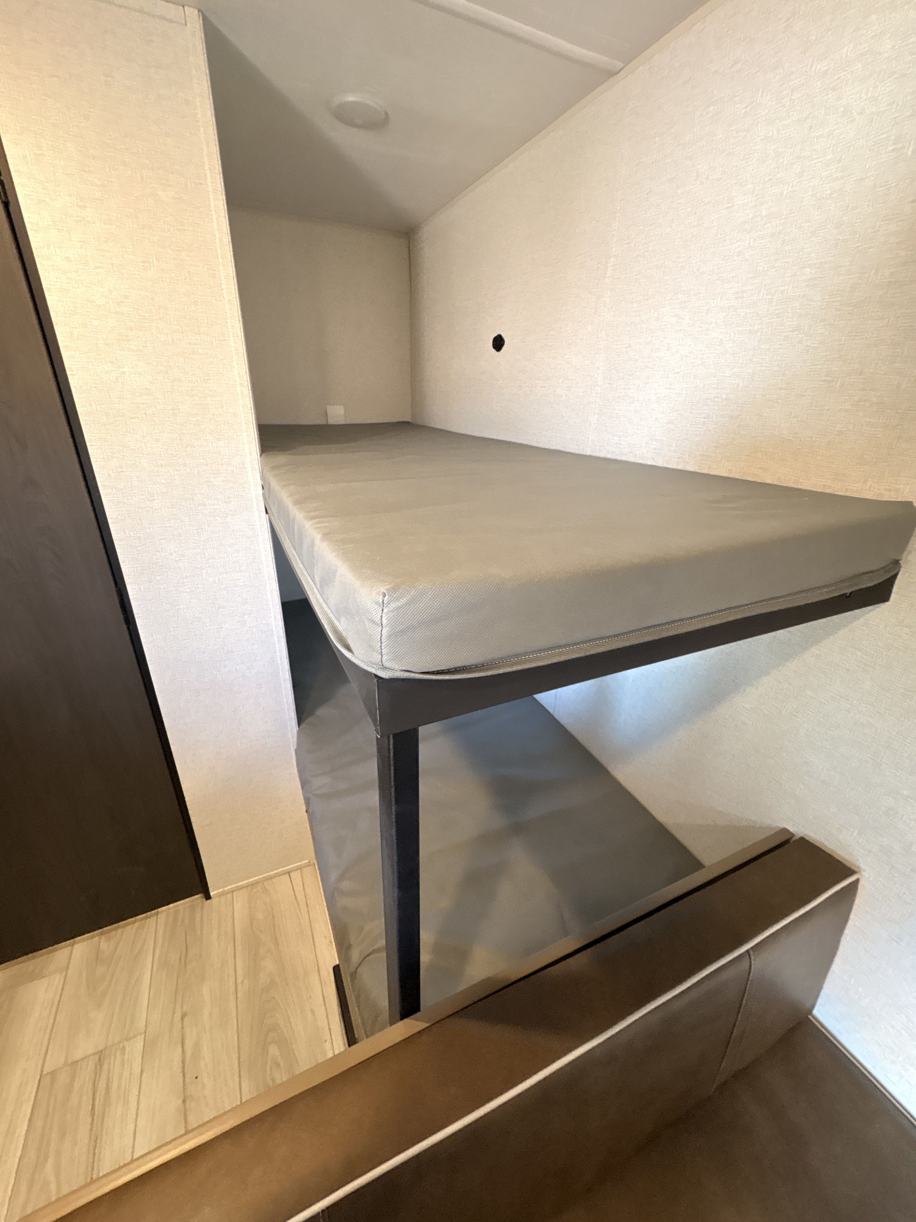 RV rental interior: compact bunk beds with gray mattresses and a brown upholstered bench, offering a snug sleeping area.. Keystone RV Springdale Mini 2025