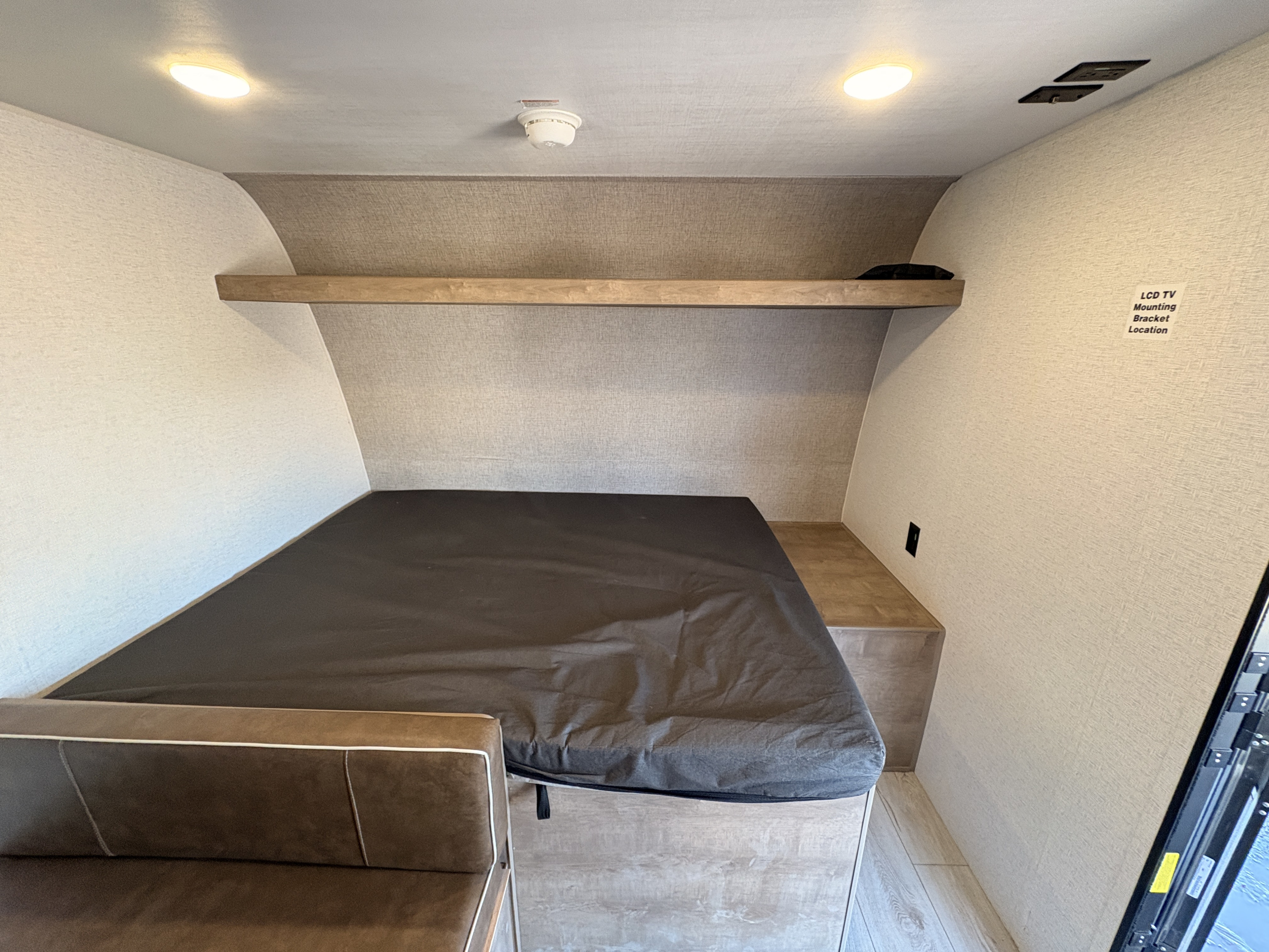 Compact RV rental sleeping area with bed, storage bench, overhead shelf, and clearly marked TV mount location.. Keystone RV Springdale Mini 2025