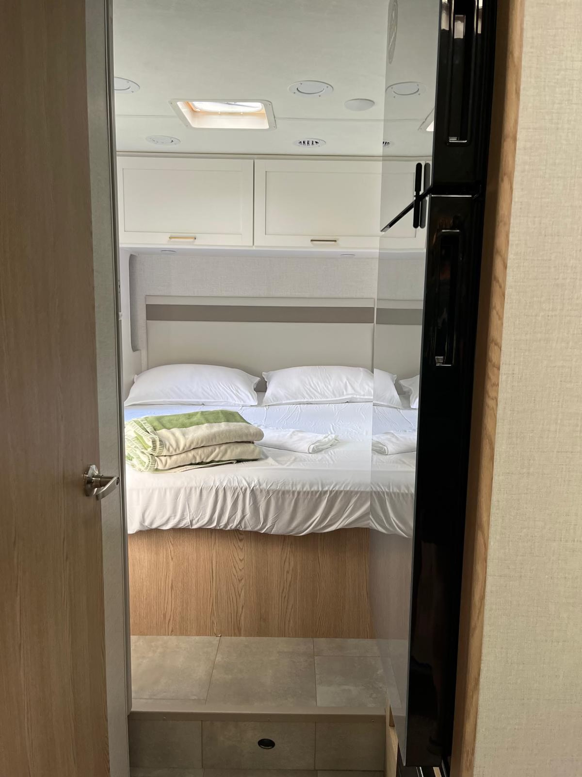Comfortable bedroom in an RV rental, featuring a made bed with fresh linens and overhead storage, viewed from a doorway.. Thor Chateau 2026