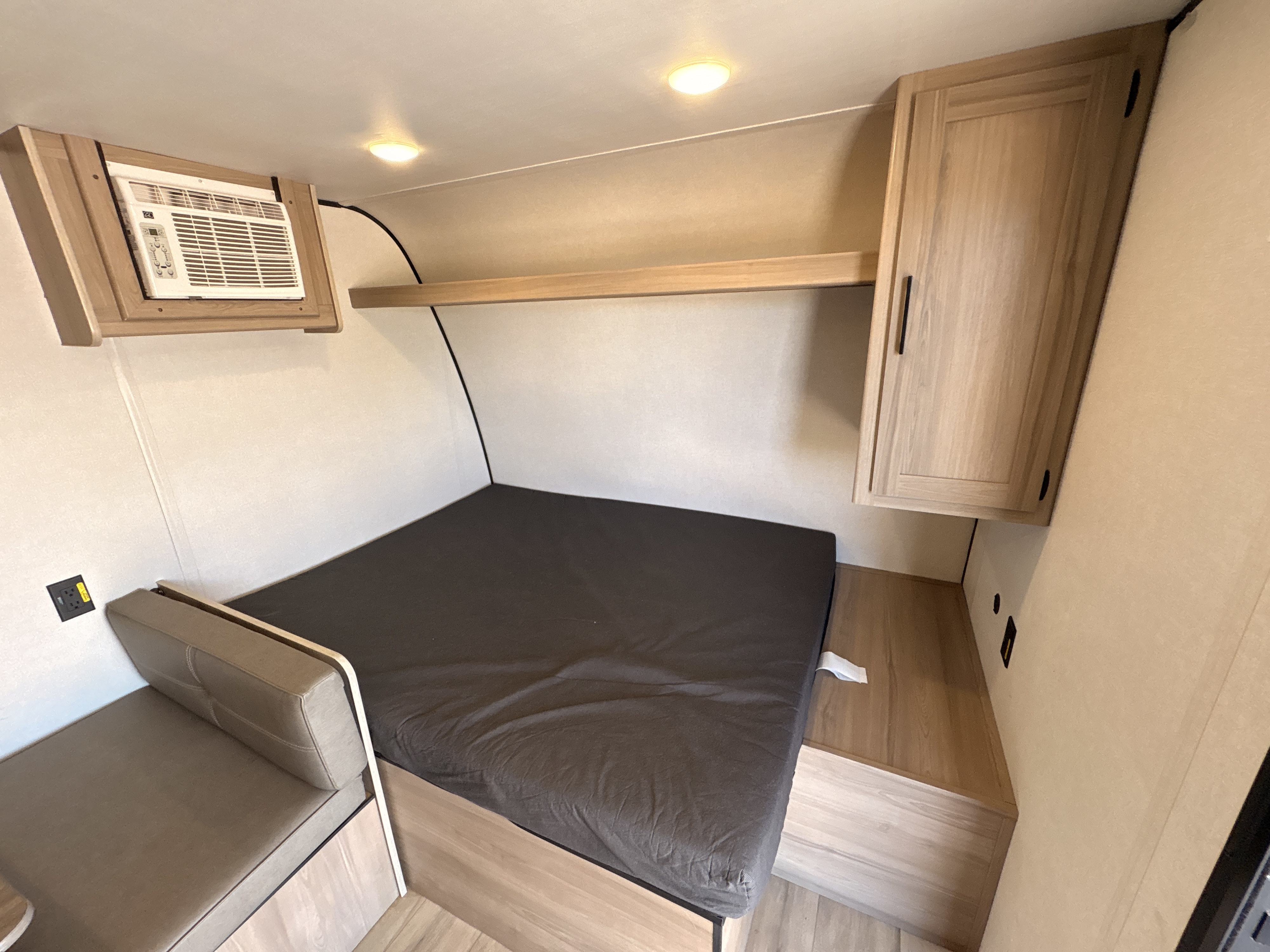 RV rental interior: A functional bedroom space with a bed, wall-mounted AC, wooden cabinet, shelf, and upholstered bench.. Keystone RV Coleman 2025