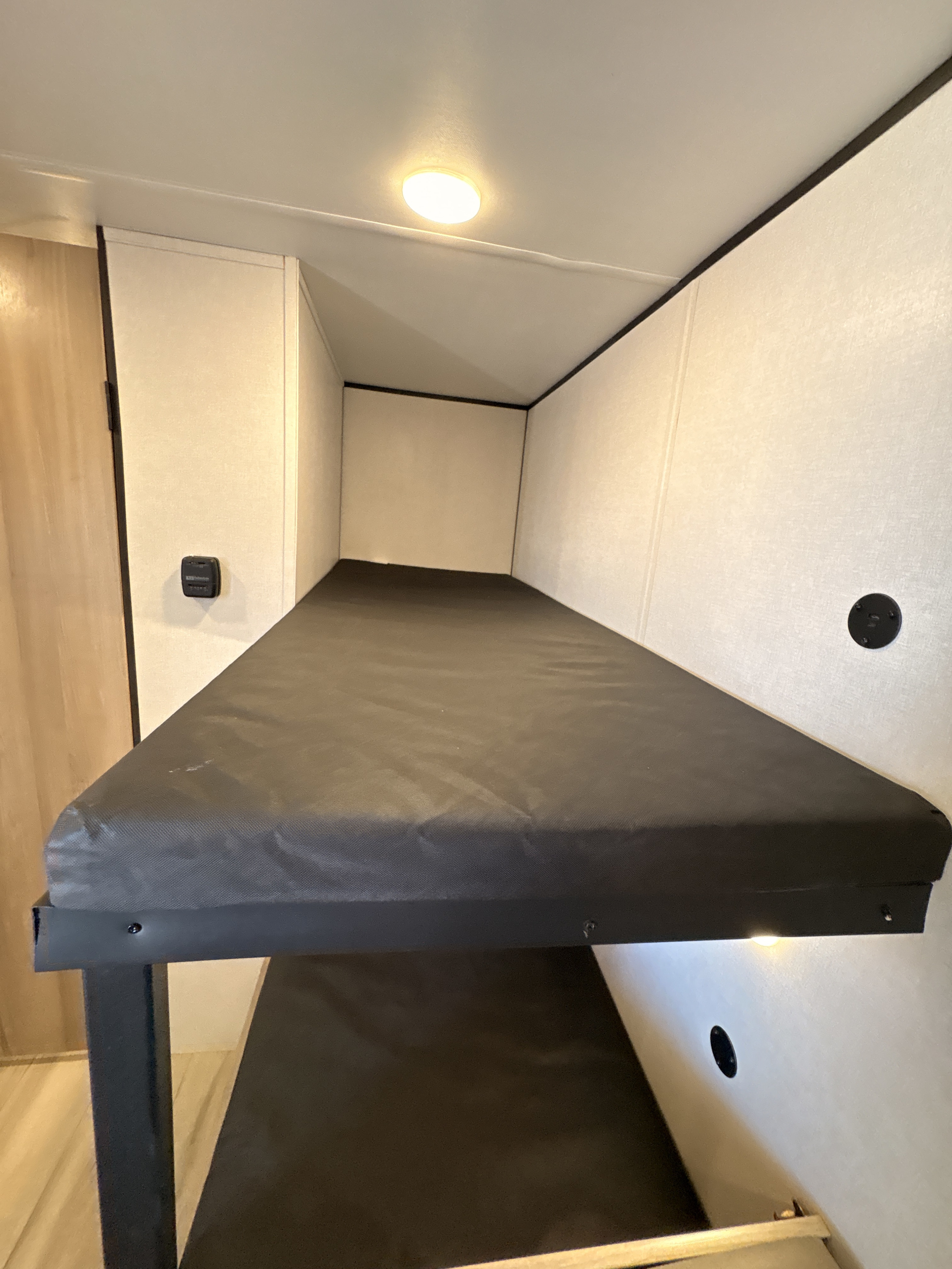 Inside an rv rental, these stacked bunk beds offer cozy sleeping with dark mattresses, a ceiling light, and wall details.. Keystone RV Coleman 2025