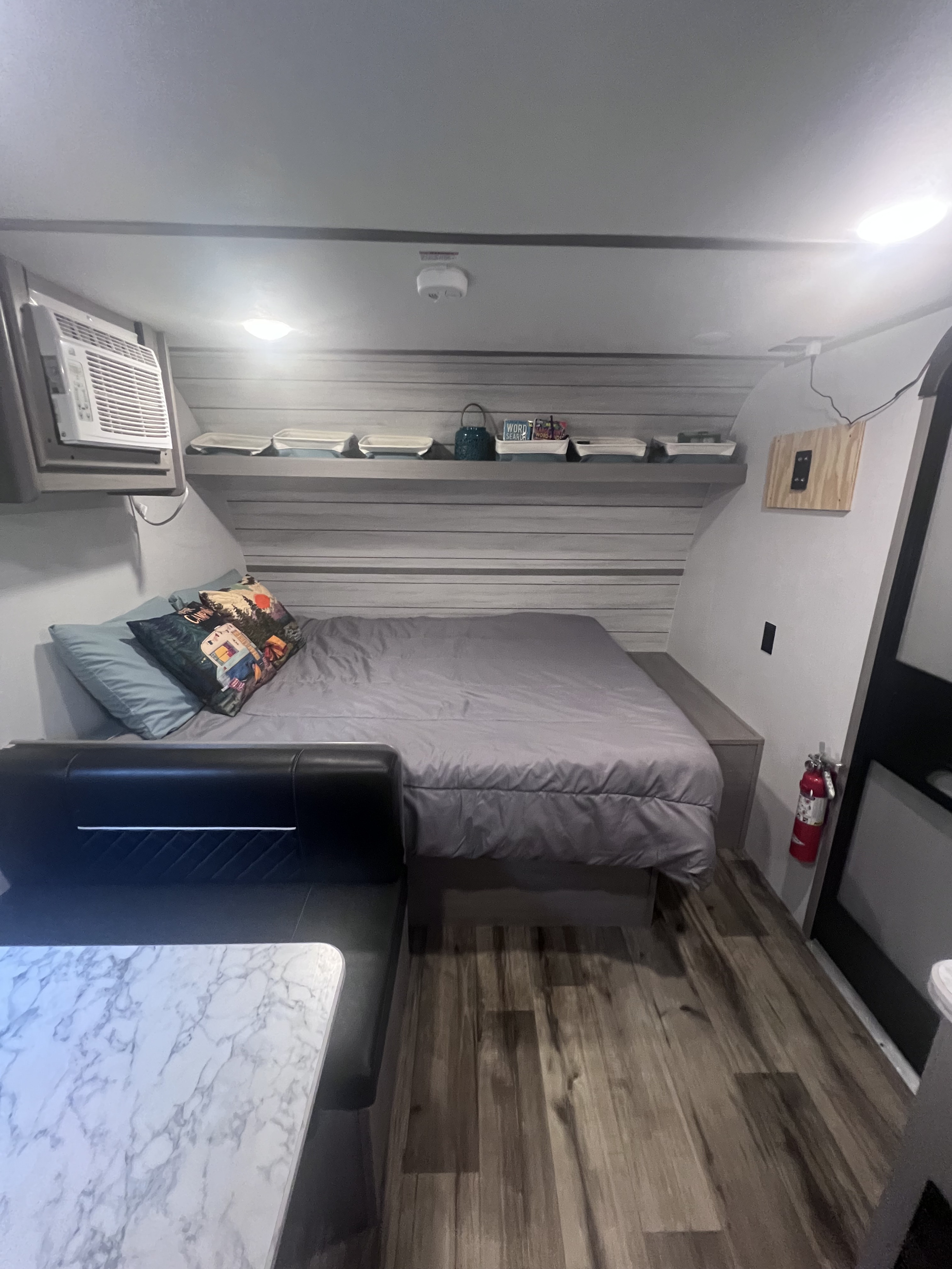 RV rental interior: cozy bed with themed pillows, AC unit, shelves, dining booth, and fire extinguisher for safety.. Keystone RV Coleman Lantern 17B 2024