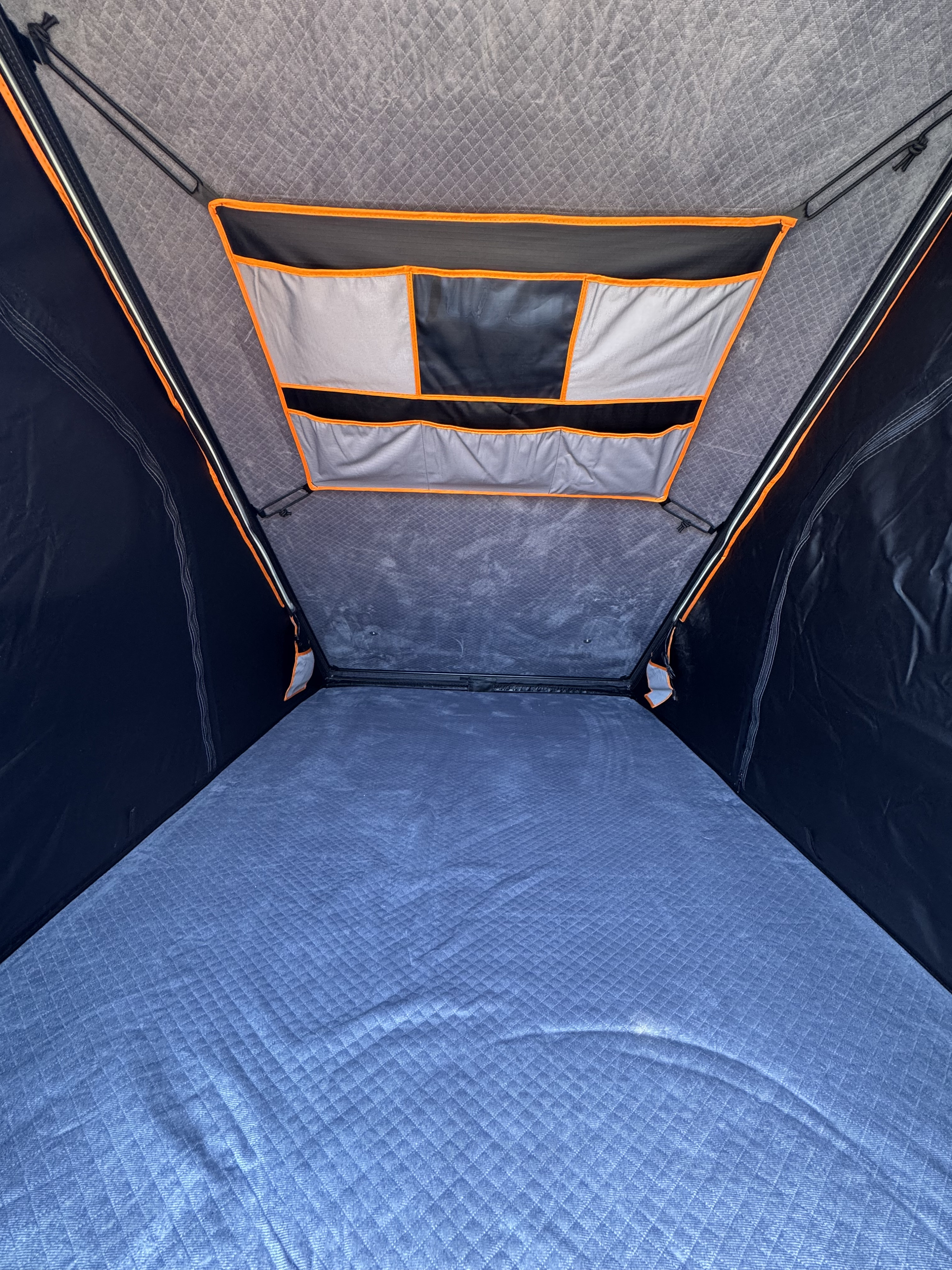 RV rental: Inside a comfortable rooftop tent, featuring a quilted blue mattress and overhead storage pockets.. Mercedes-Benz Sprinter 2024