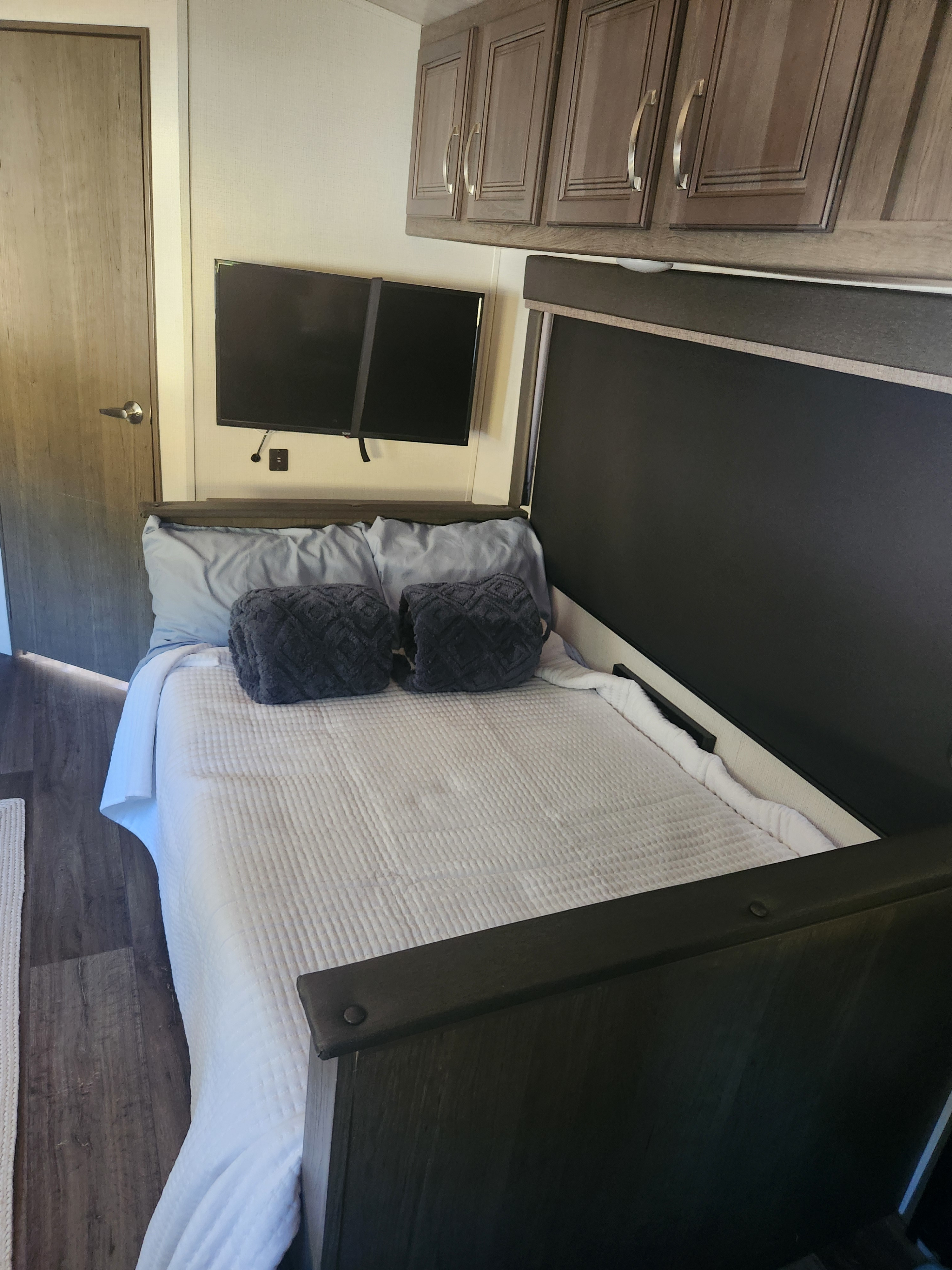 Cozy rv rental bedroom featuring a comfortable bed, wall-mounted TV, wooden cabinets, and a compact design.. Keystone RV Cougar 2023