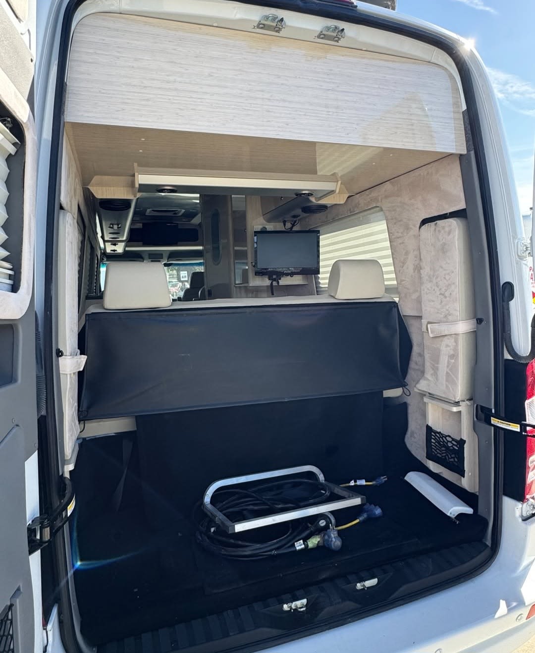 Inside this RV rental's rear: bed, mounted TV, and lower storage with utility cords. Camper van living space.. Airstream Interstate 2013