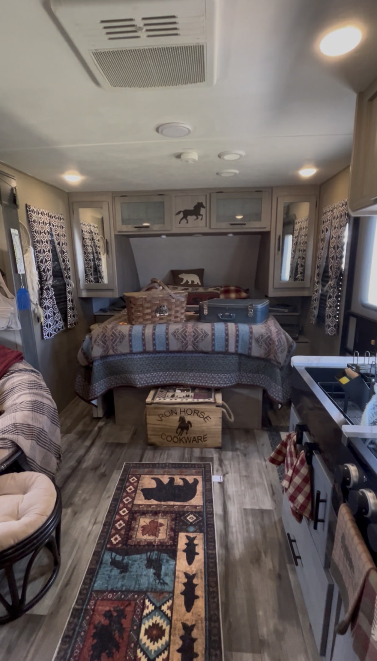 RV rental bedroom & kitchen: rustic decor, patterned quilt, nature rug, and overhead AC unit in a cozy interior.. Dutchmen Coleman Light 2023