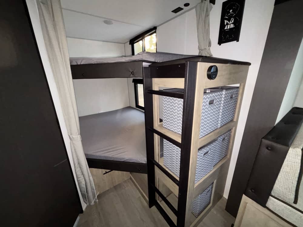 RV rental bunk beds offer cozy sleeping space with smart, chevron-patterned storage bins integrated into the interior design.. Forest River Campsite Reserve 2026