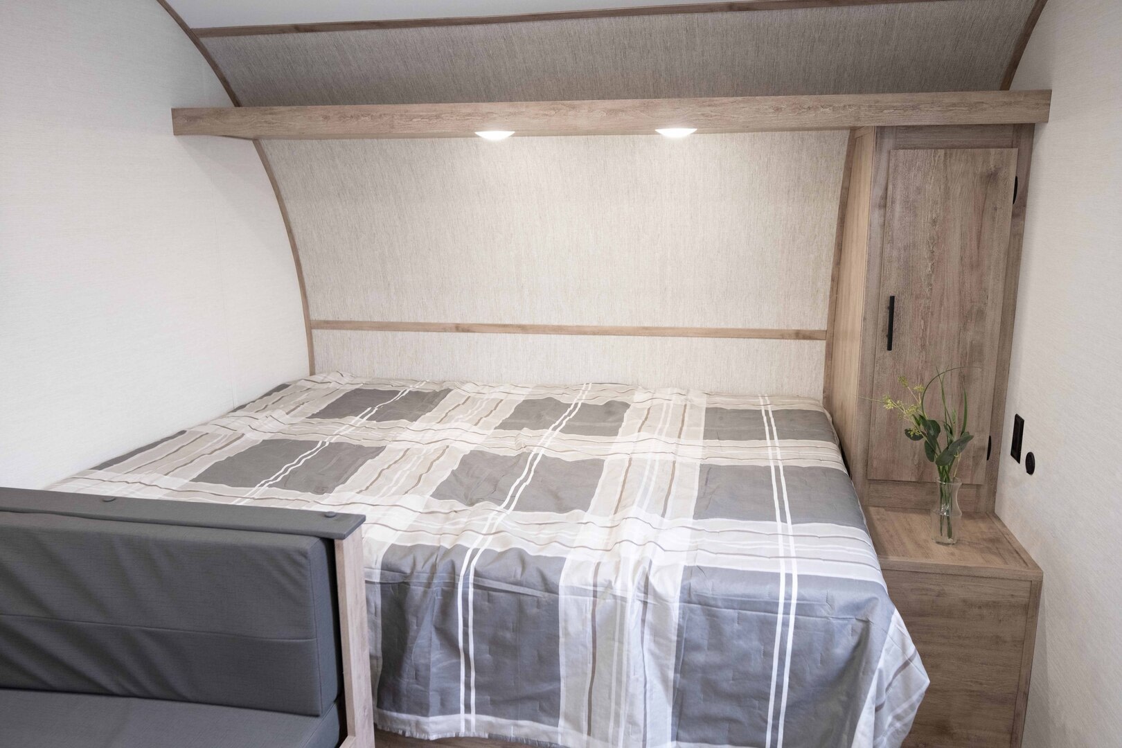 Comfortable RV rental bedroom with a grey plaid bed, built-in cabinet, and overhead reading lights.. Gulf Stream Ameri-Lite 2026