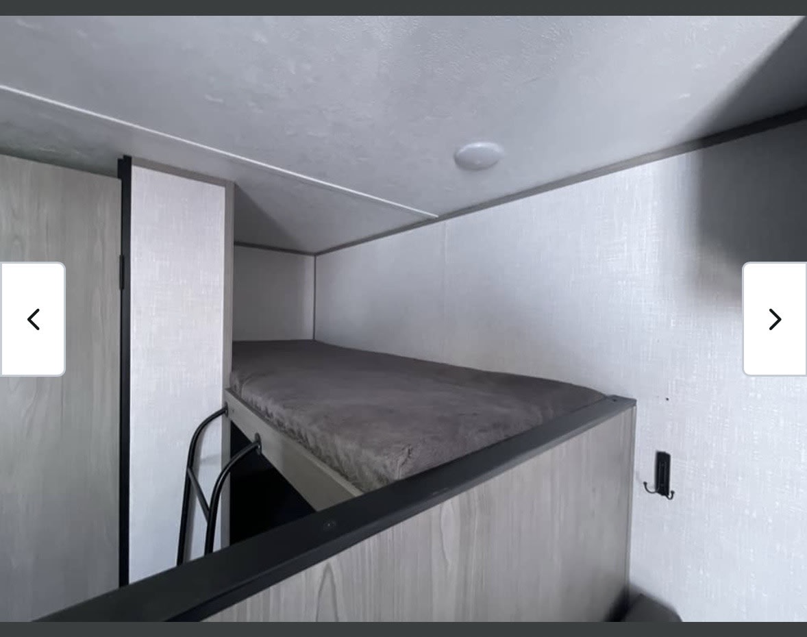Cozy RV rental bunk beds, featuring a lower bunk with a gray mattress, ladder, light walls & ceiling. Ideal for travel.. Dutchmen Coleman Lantern LT 2022