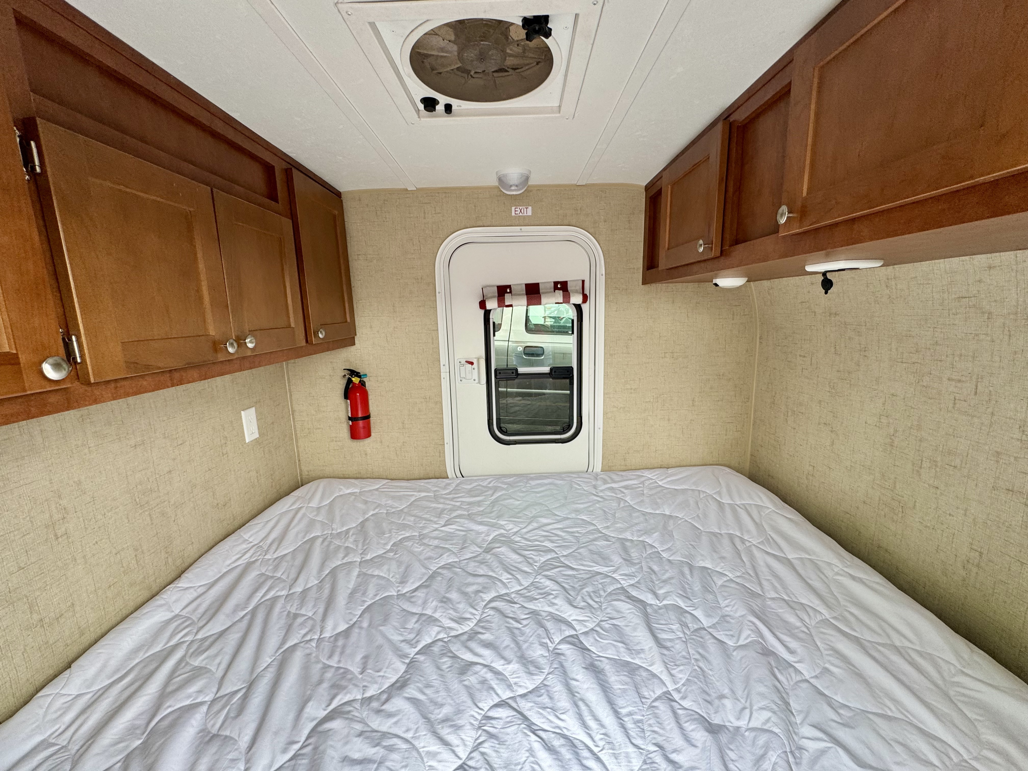 Cozy RV rental interior: large bed, wooden cabinets, ceiling fan, exit door, and fire extinguisher for safety.. Riverside RV White Water 2016
