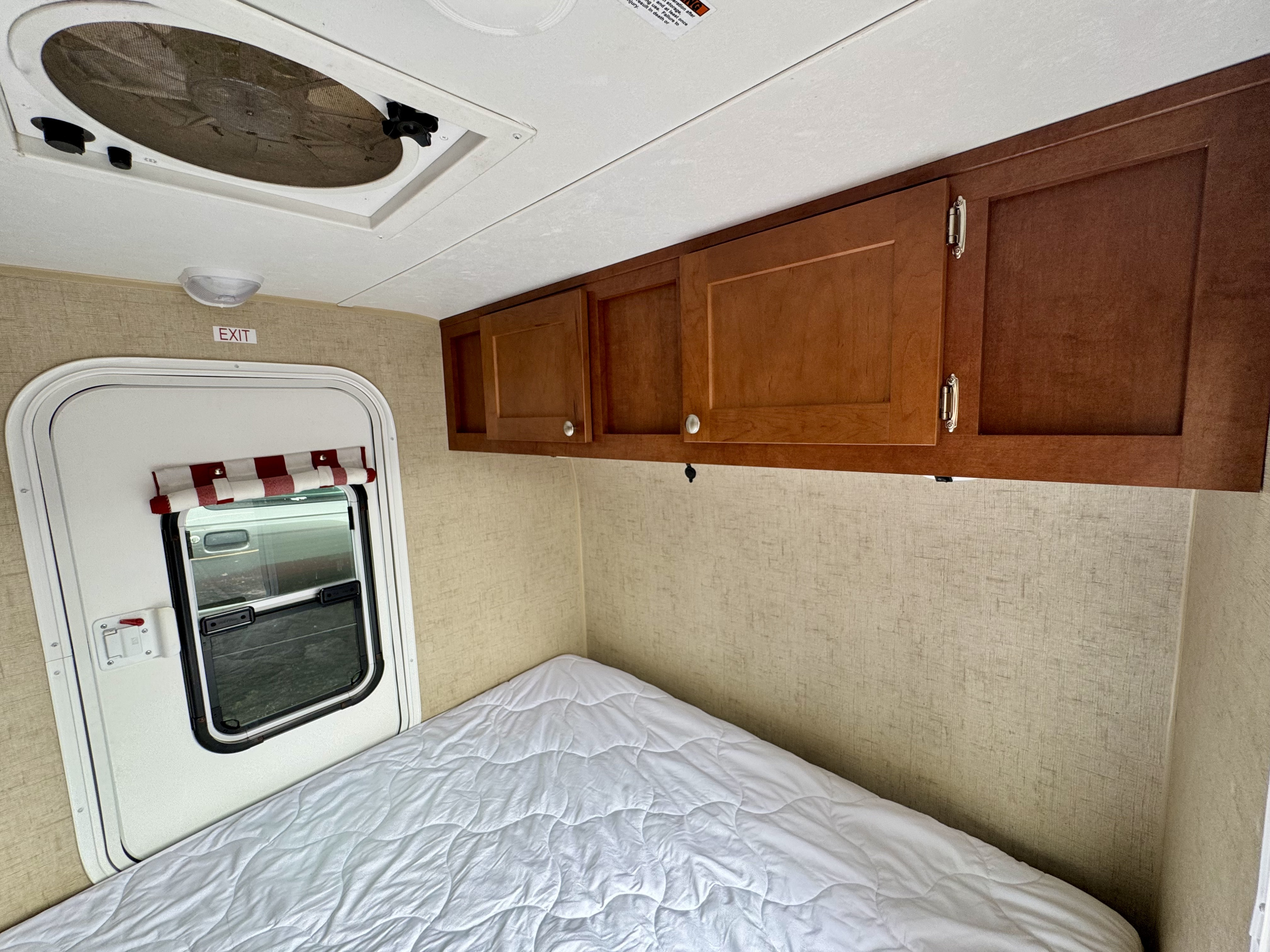 RV rental bedroom featuring a comfy bed, overhead storage cabinets, an exit door, and a ceiling fan.. Riverside RV White Water 2016