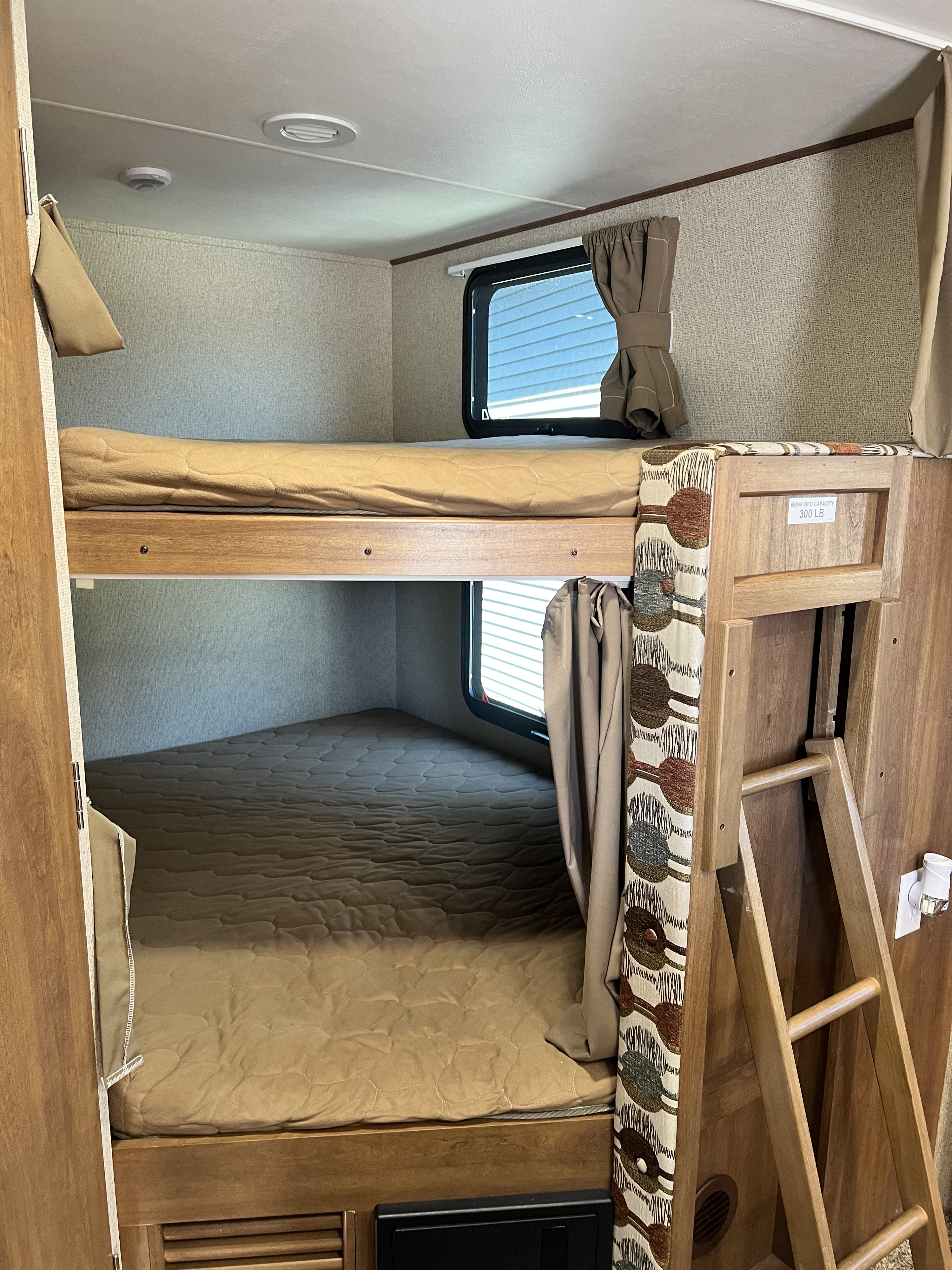 RV rental bunk beds with ladder, windows, and tan bedding, showing upper and lower bunks for comfortable travel.. Coachmen Apex 2018